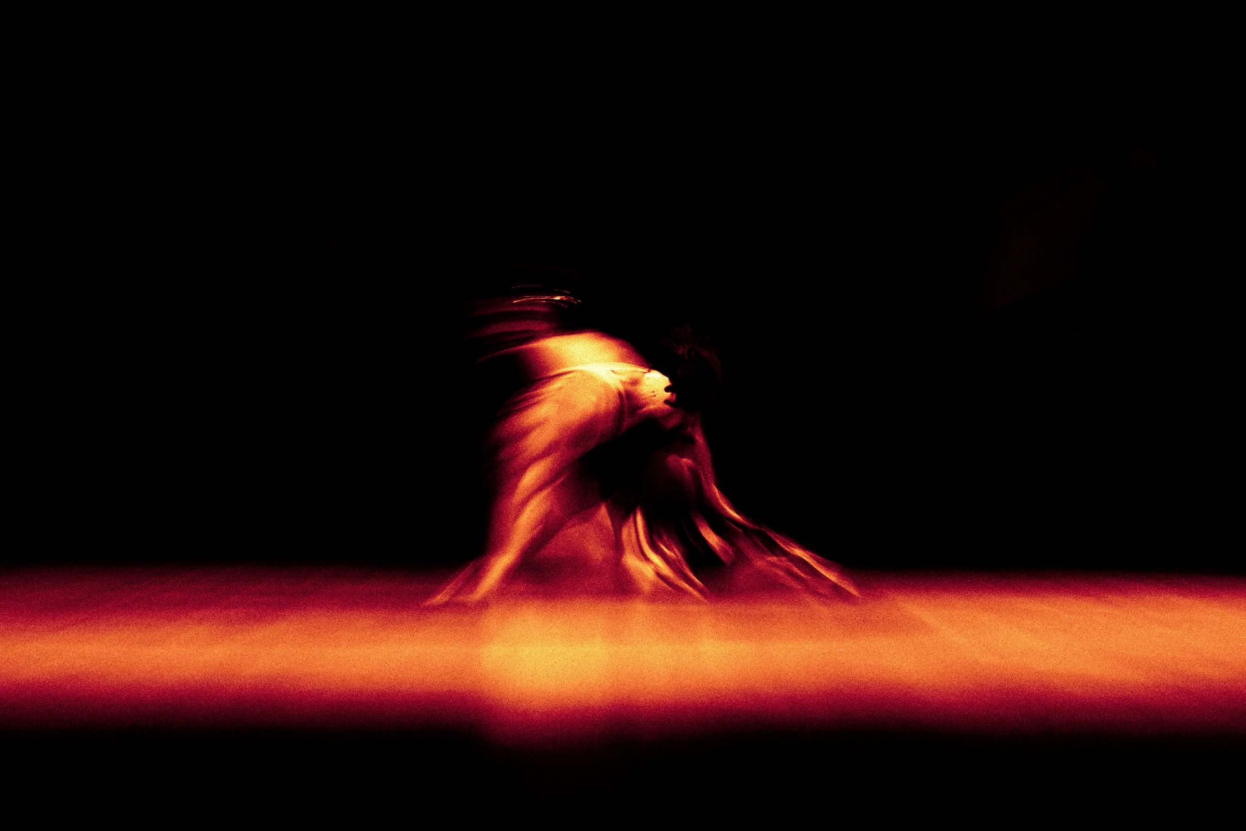 A person dancing in a flowing dress illuminated by warm stage lighting with a dark background.