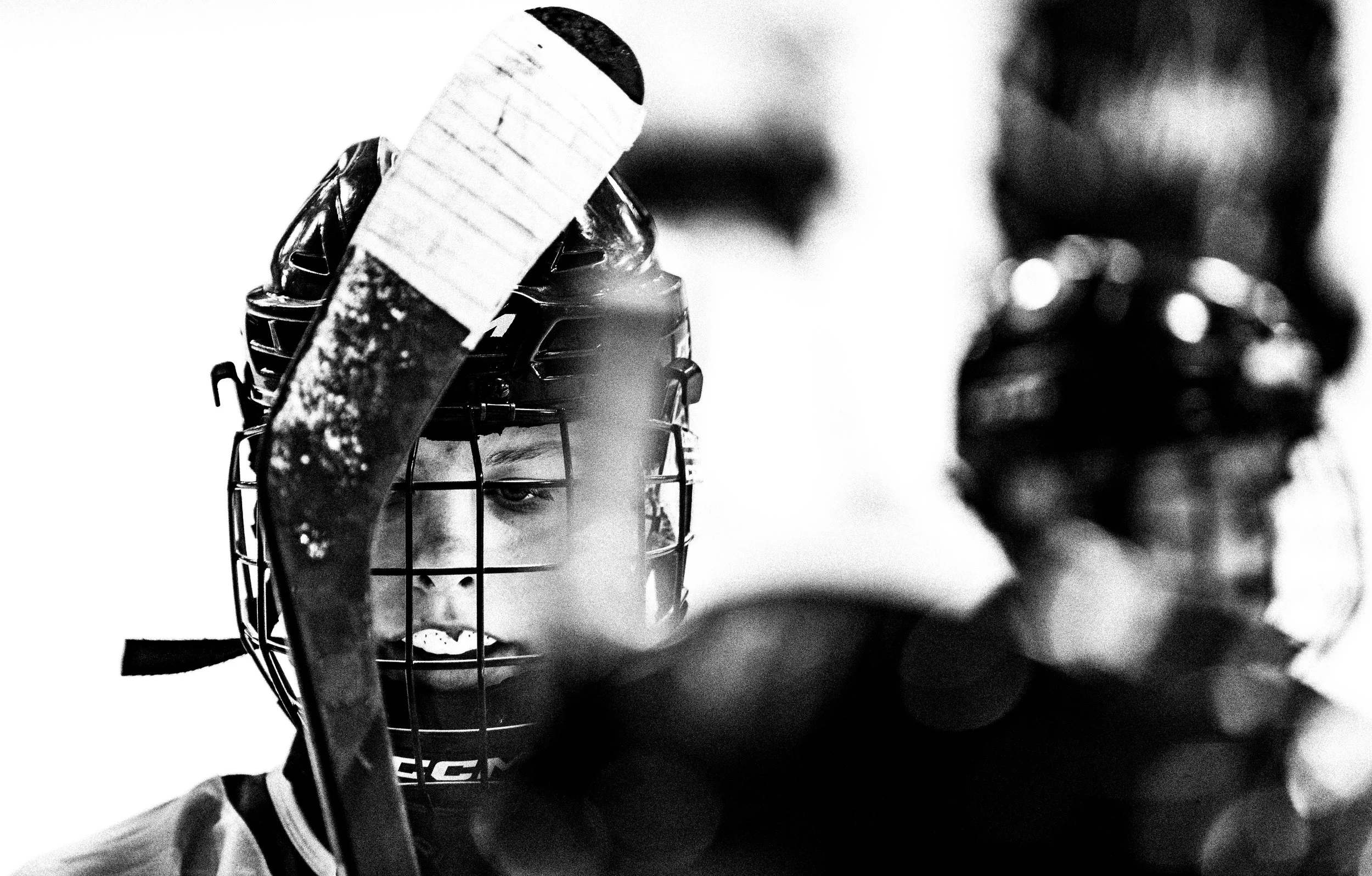 Close-up black and white photo of a hockey goalie with a face mask and holding a hockey stick.