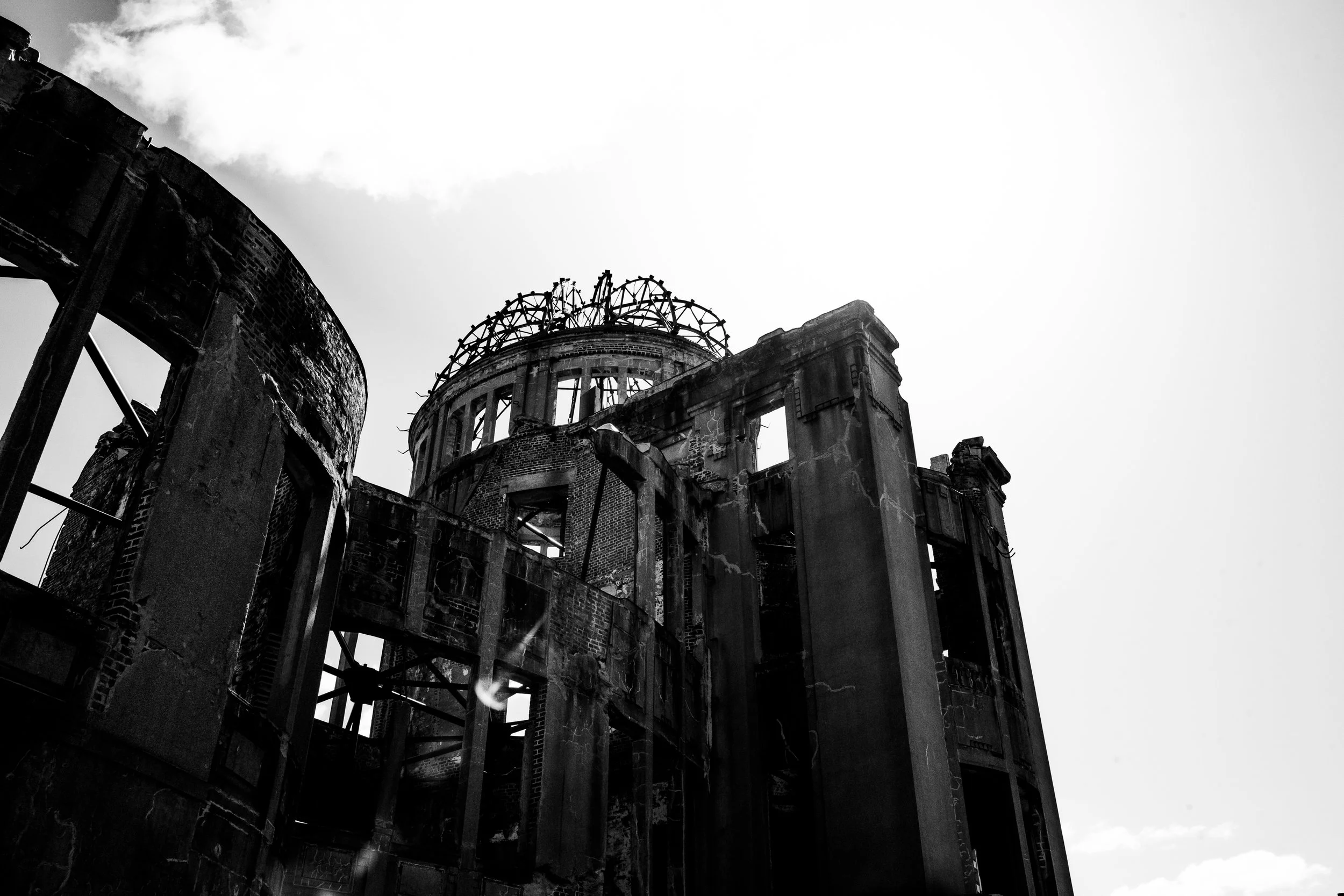Ruined, burned-out building with exposed metal framework and damaged brick walls, under a cloudy sky.