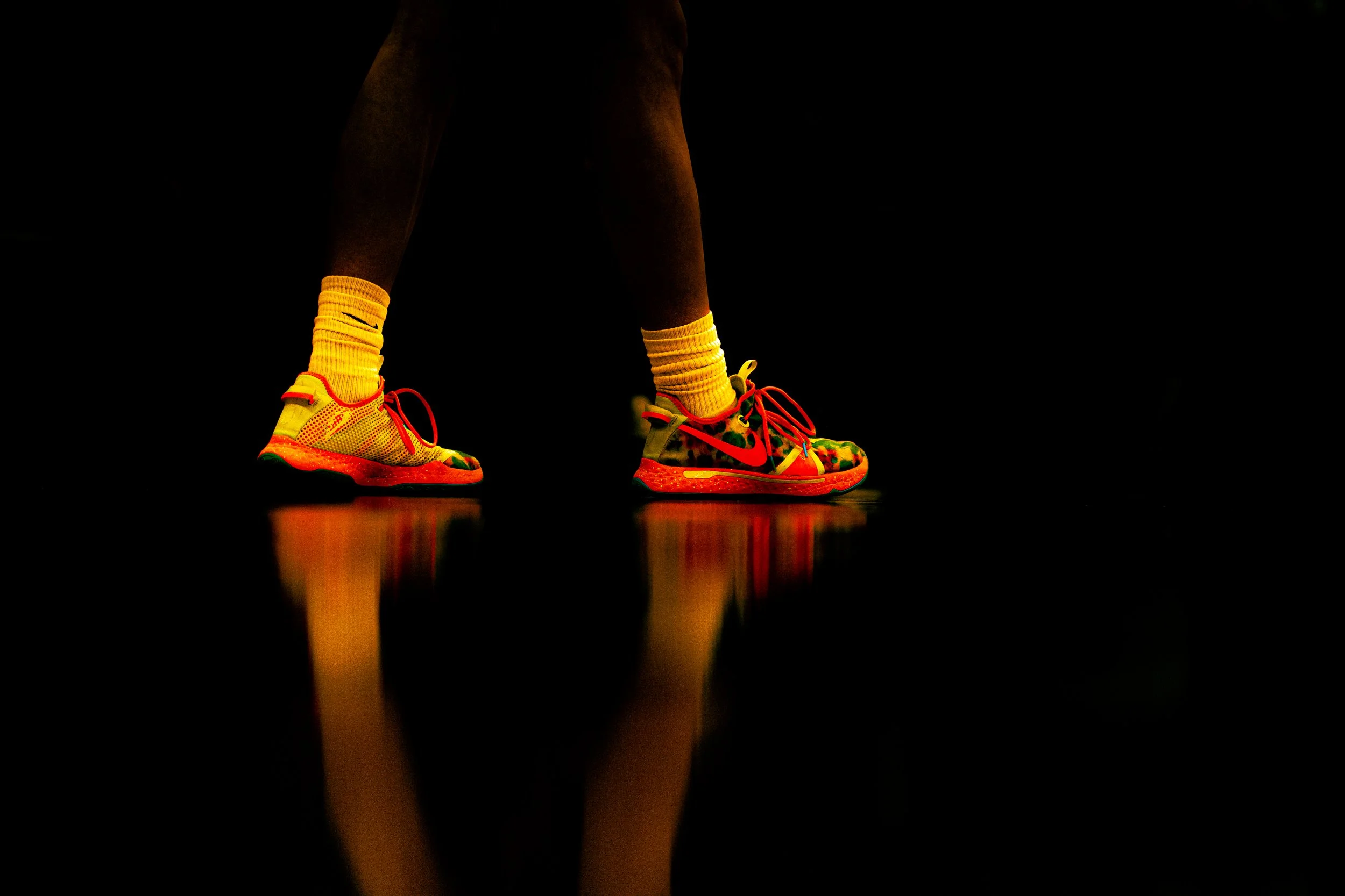 Close-up of a person's lower legs and feet wearing bright yellow socks and colorful running shoes against a dark background.