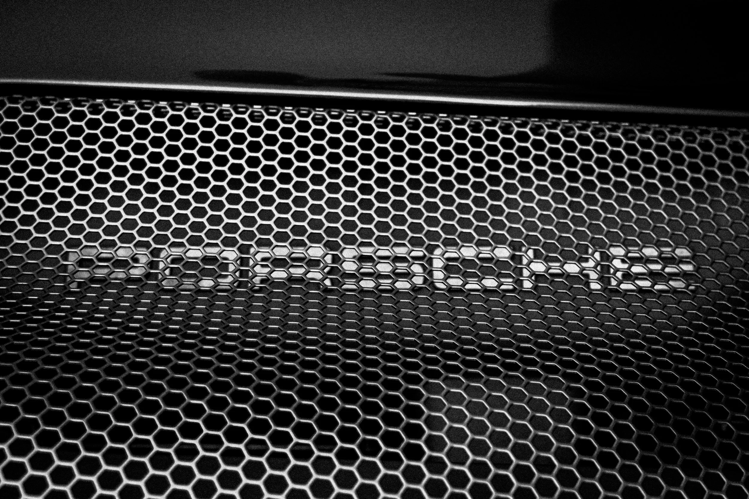 Close-up of a metallic honeycomb grill pattern on a black surface.