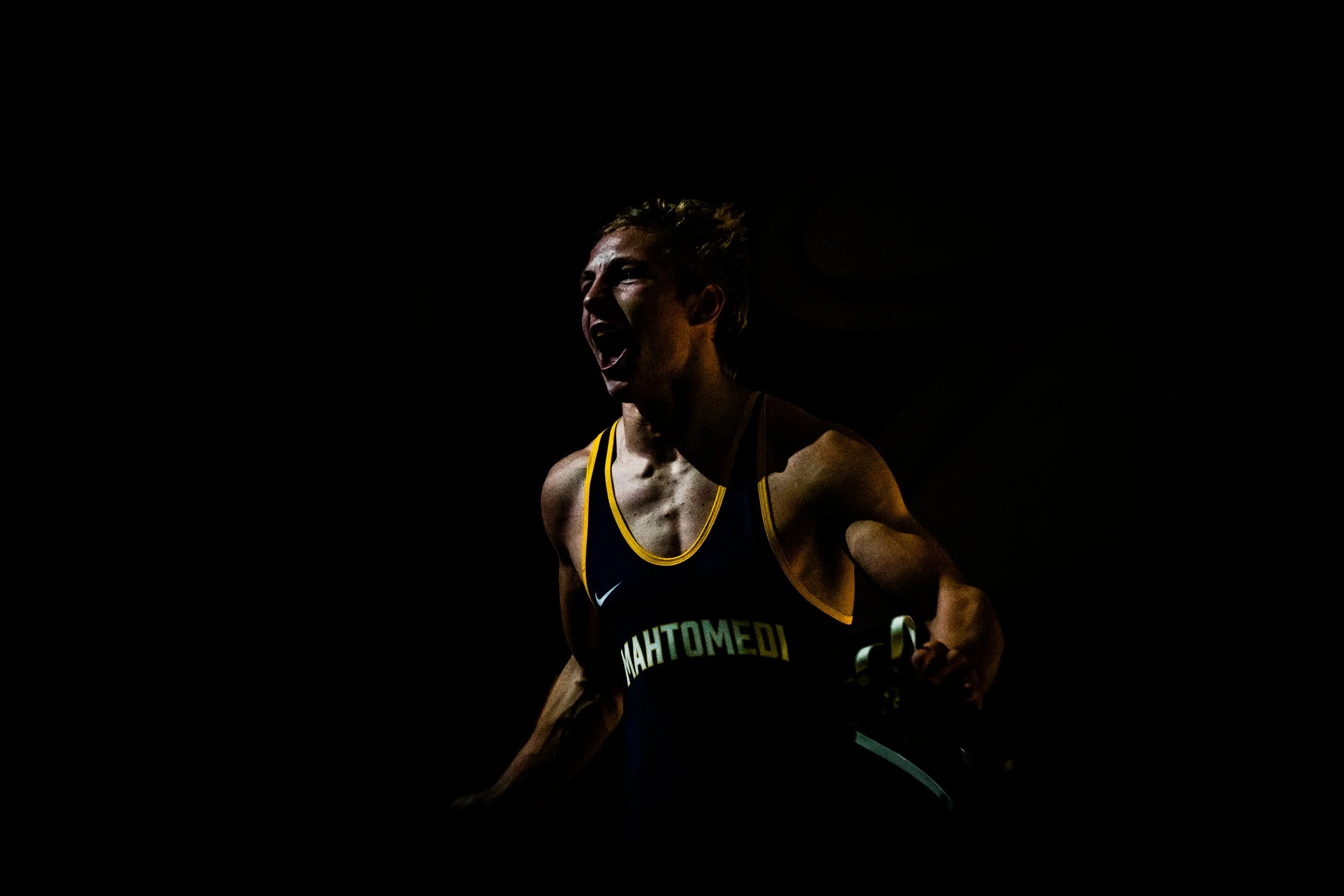 A person in a sports uniform appears to be celebrating or shouting, captured in a dark setting with dramatic lighting highlighting their face and upper body.