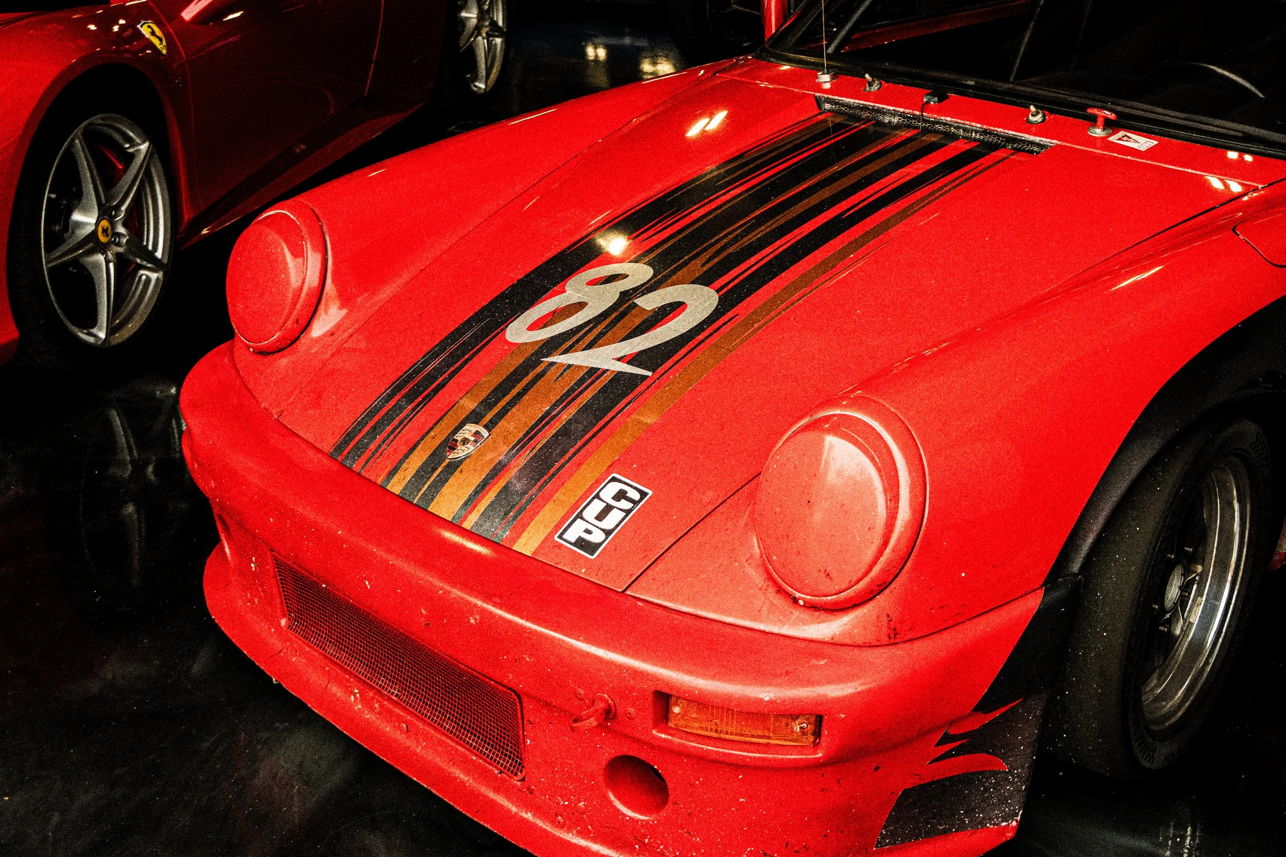 Red vintage race car with black and gold striped design on the hood, displaying the number 80 and Porsche logo.