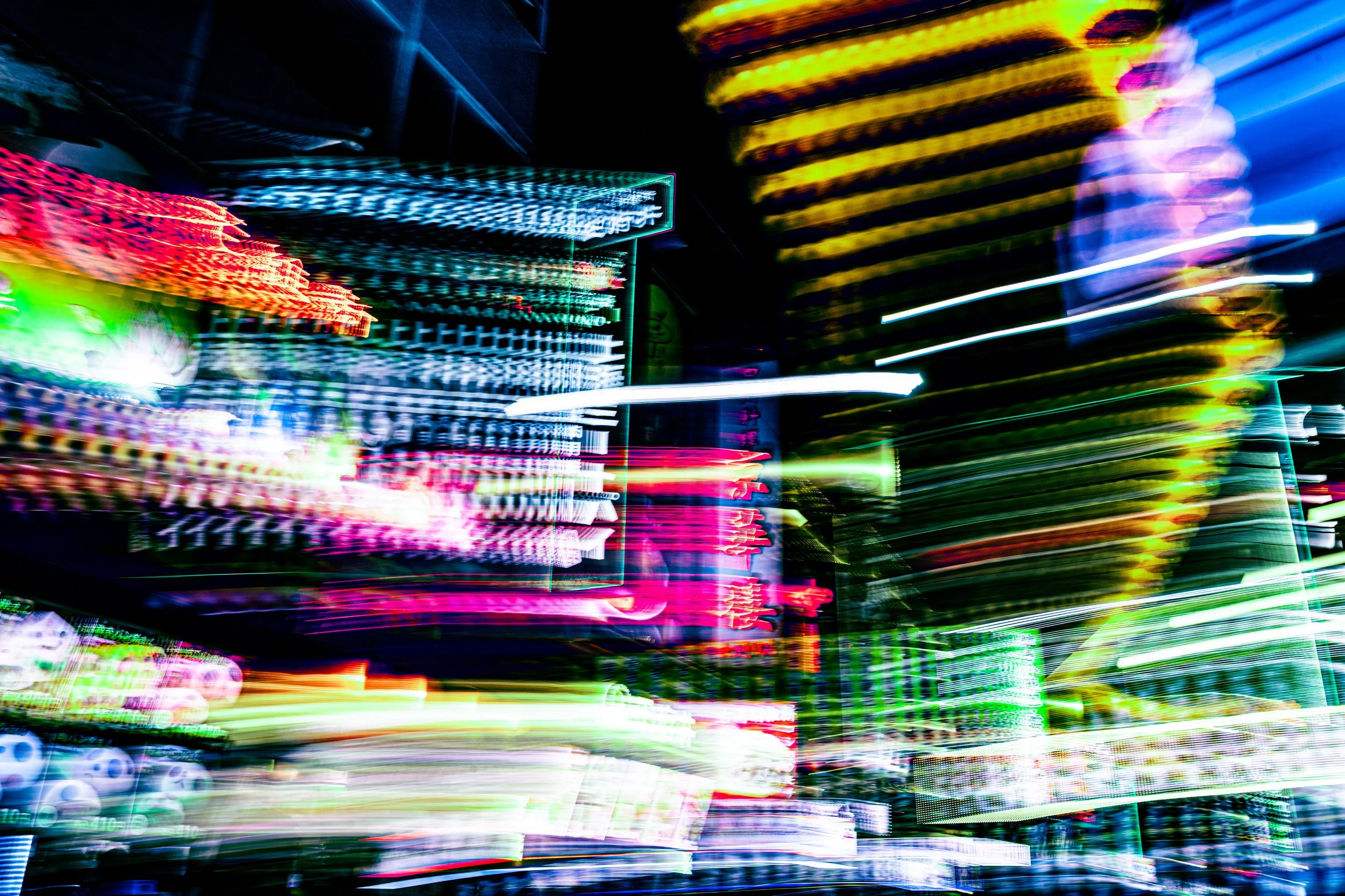 A vibrant display of multicolored neon lights and blurred signage at a nighttime urban scene, creating a dynamic and colorful abstract effect.