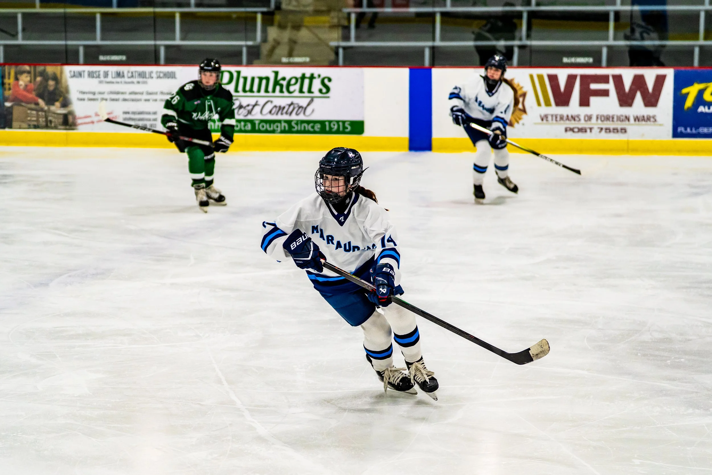 Young hockey players in uniforms and helmets skating on ice rink during a game.