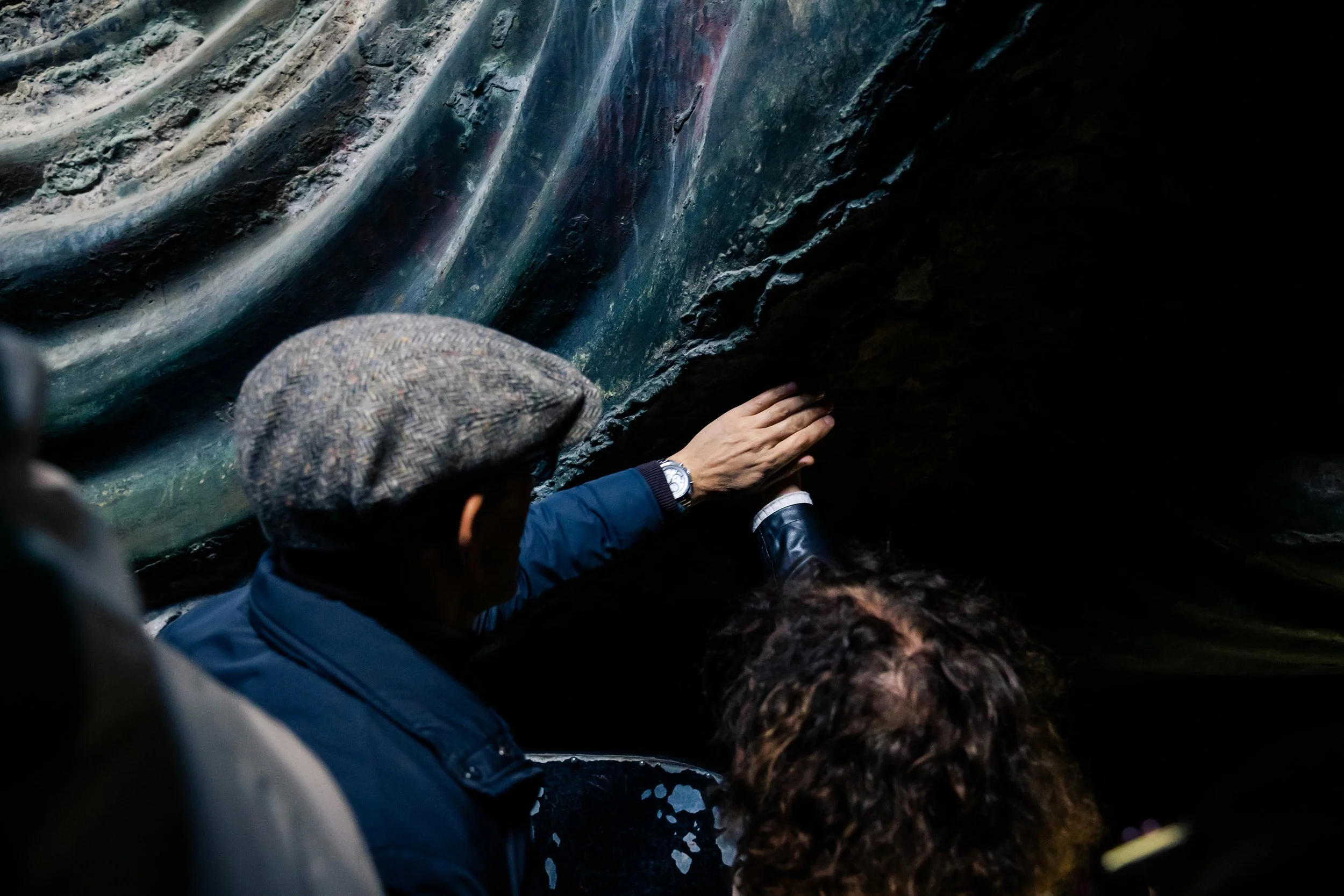 People in warm clothing exploring a dark, narrow cave or tunnel with textured, uneven walls.