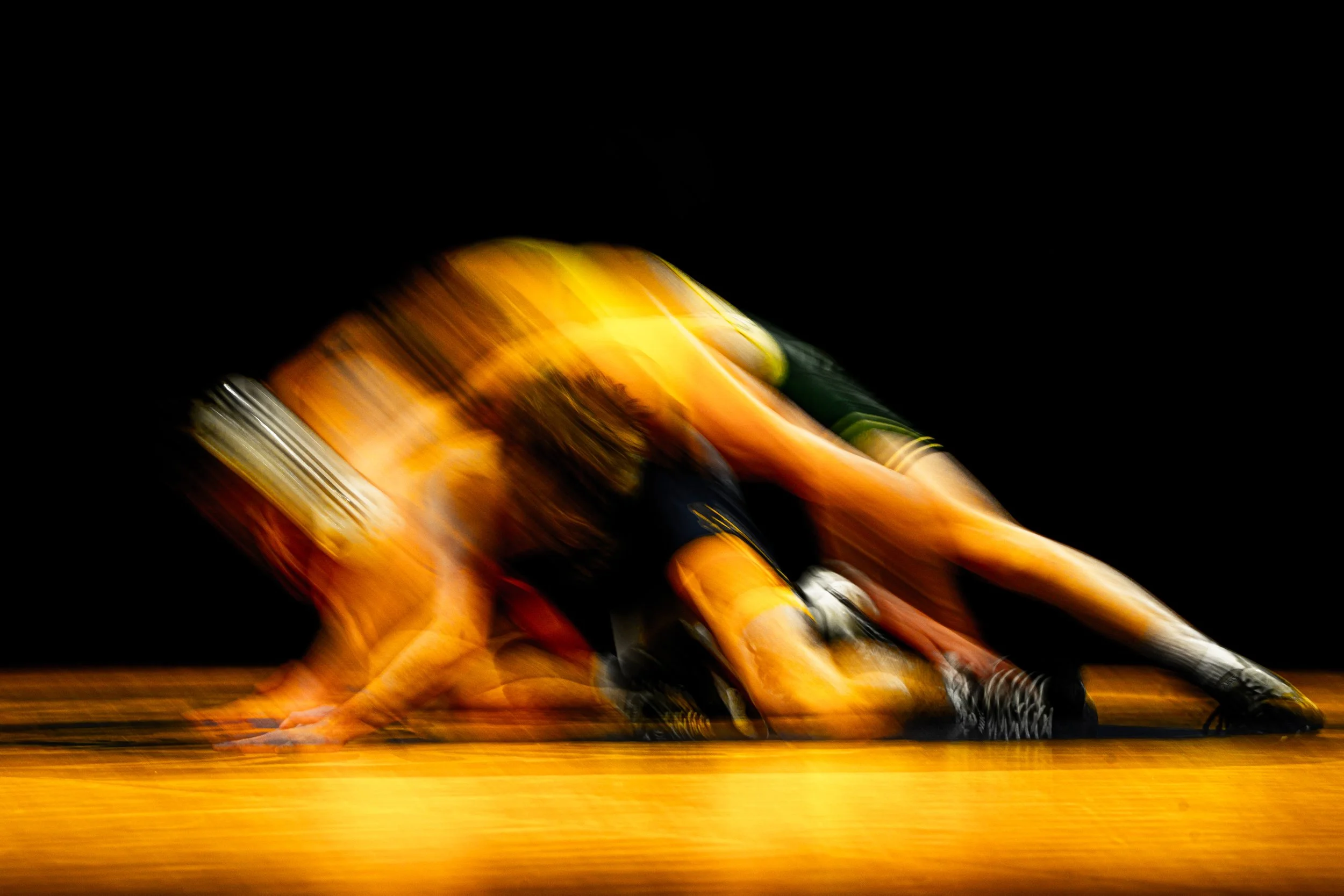 Blurred image of a running athlete in a yellow uniform on a wooden track against a dark background.