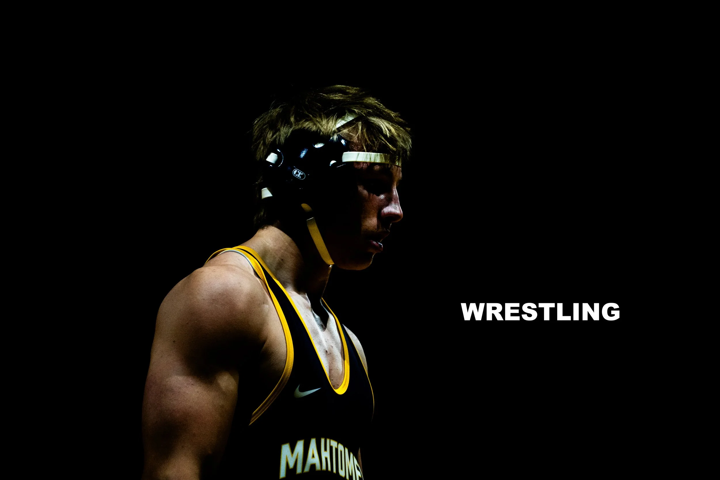 A female wrestler wearing a black helmet with white accents, a black and yellow wrestling singlet, and a serious expression features in a dark background with the word 'WRESTLING' in white text.