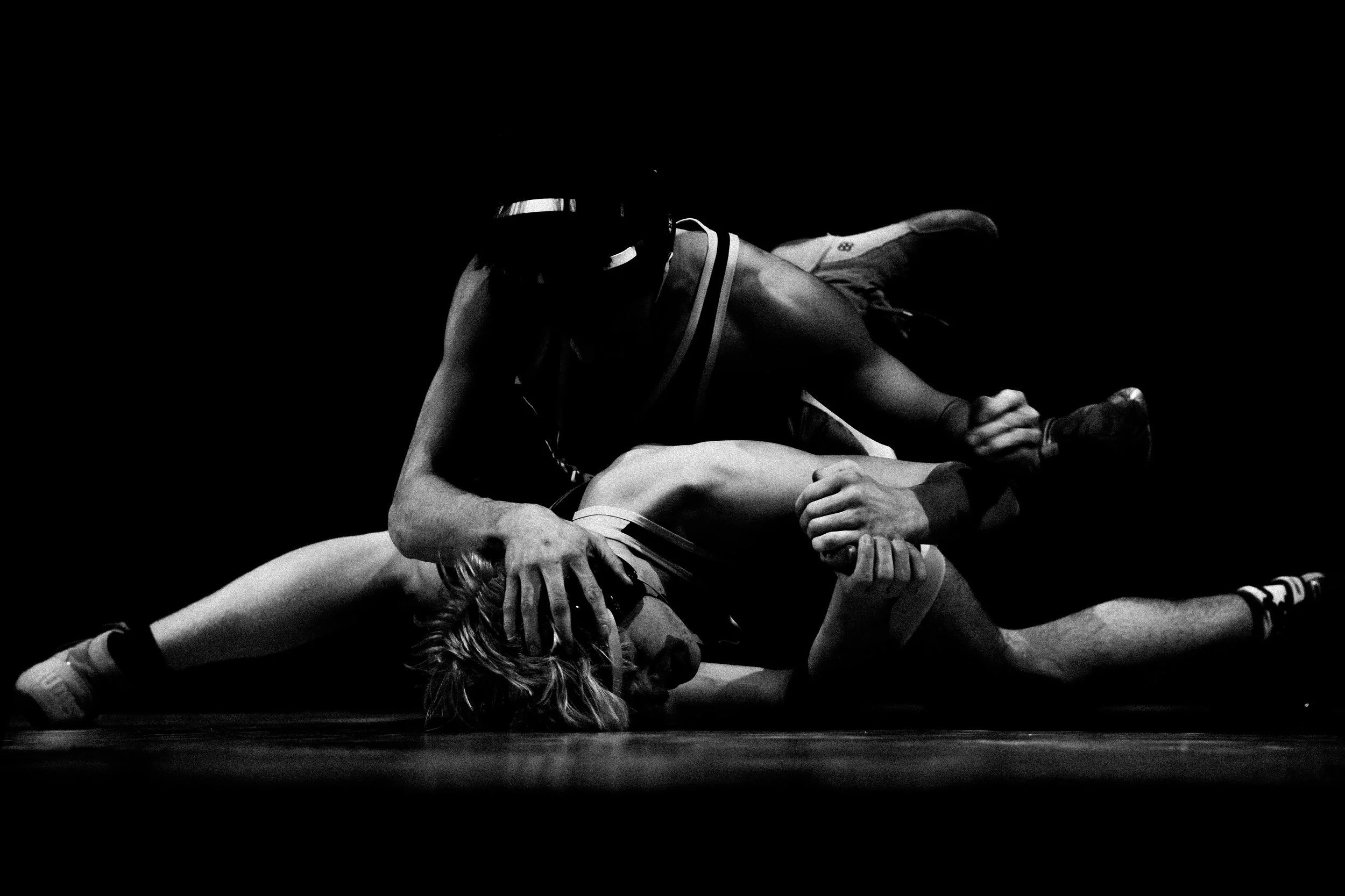 Two wrestlers engaged in a match, one in a dominant position on top of the other on a wrestling mat, black and white photo.