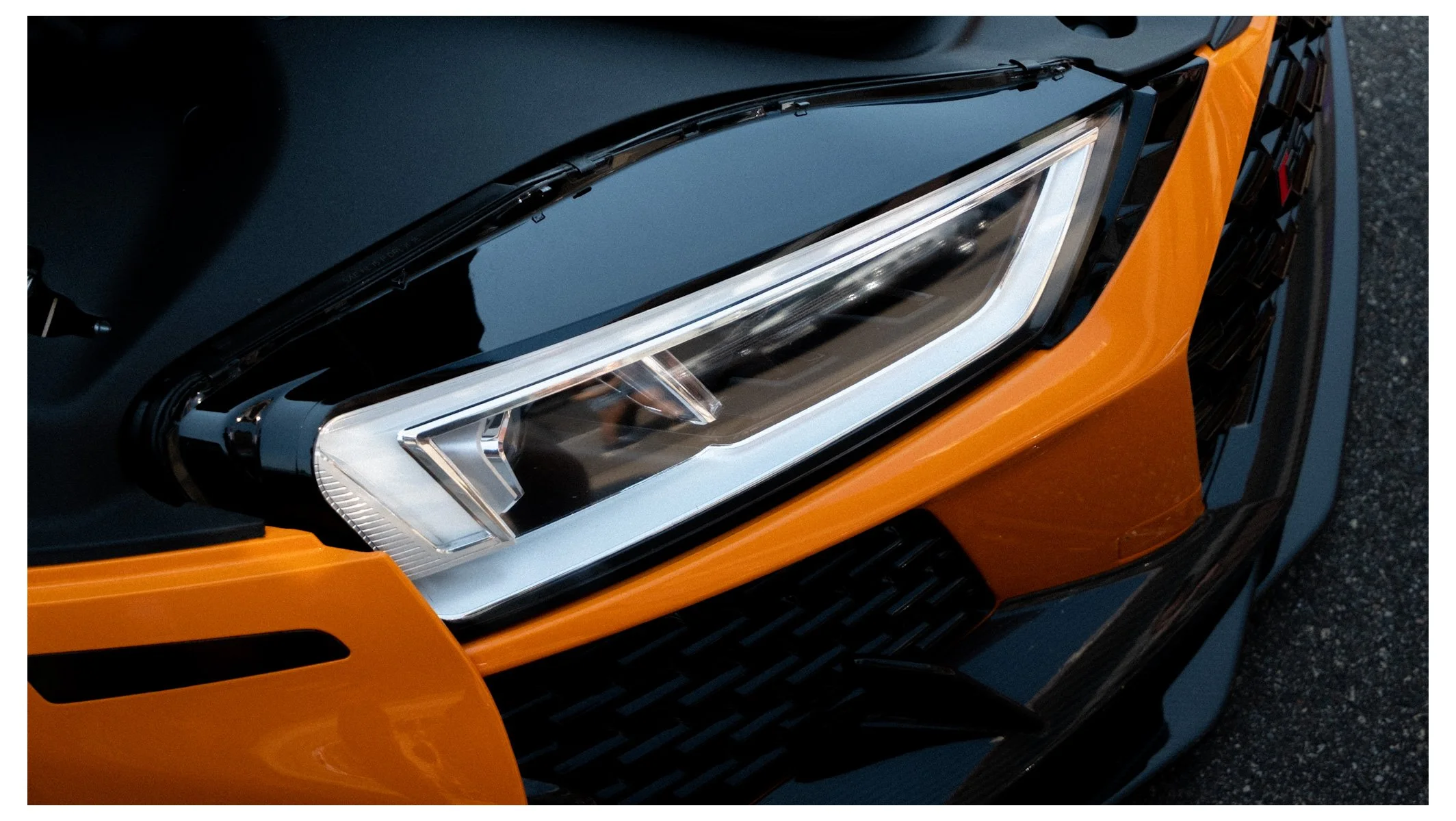 Close-up of a modern car's headlight on an orange vehicle, showing the sleek design and LED lights, with black grille detail nearby.