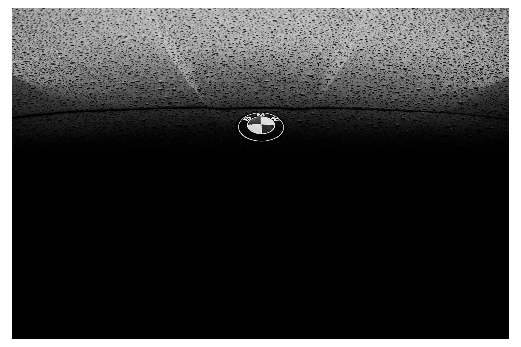 Close-up of a BMW car hood covered with water droplets, with BMW logo in the center.
