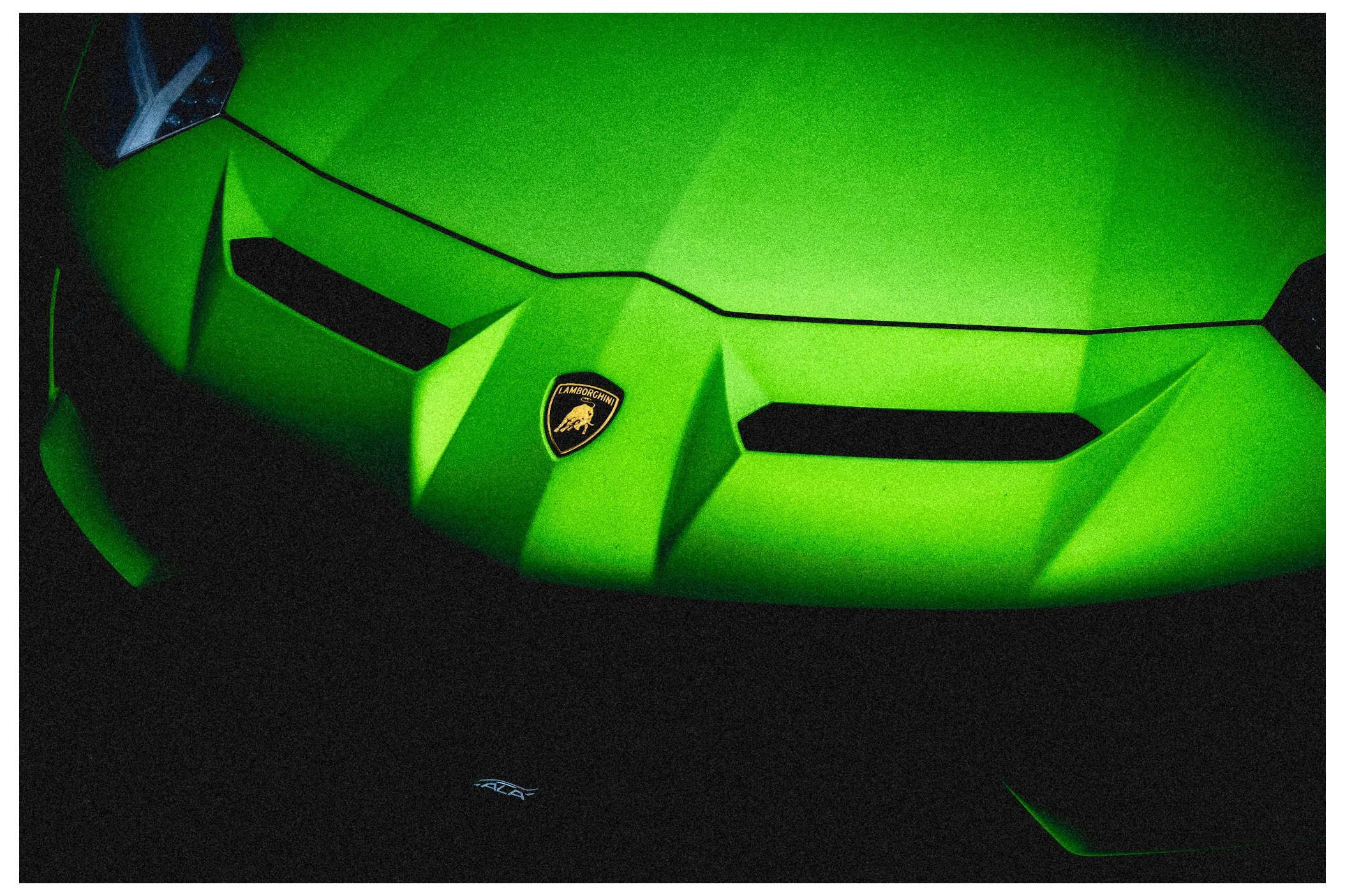 A bright green Lamborghini sports car with the Lamborghini emblem on the front, photographed in a dark setting with subtle lighting highlights.