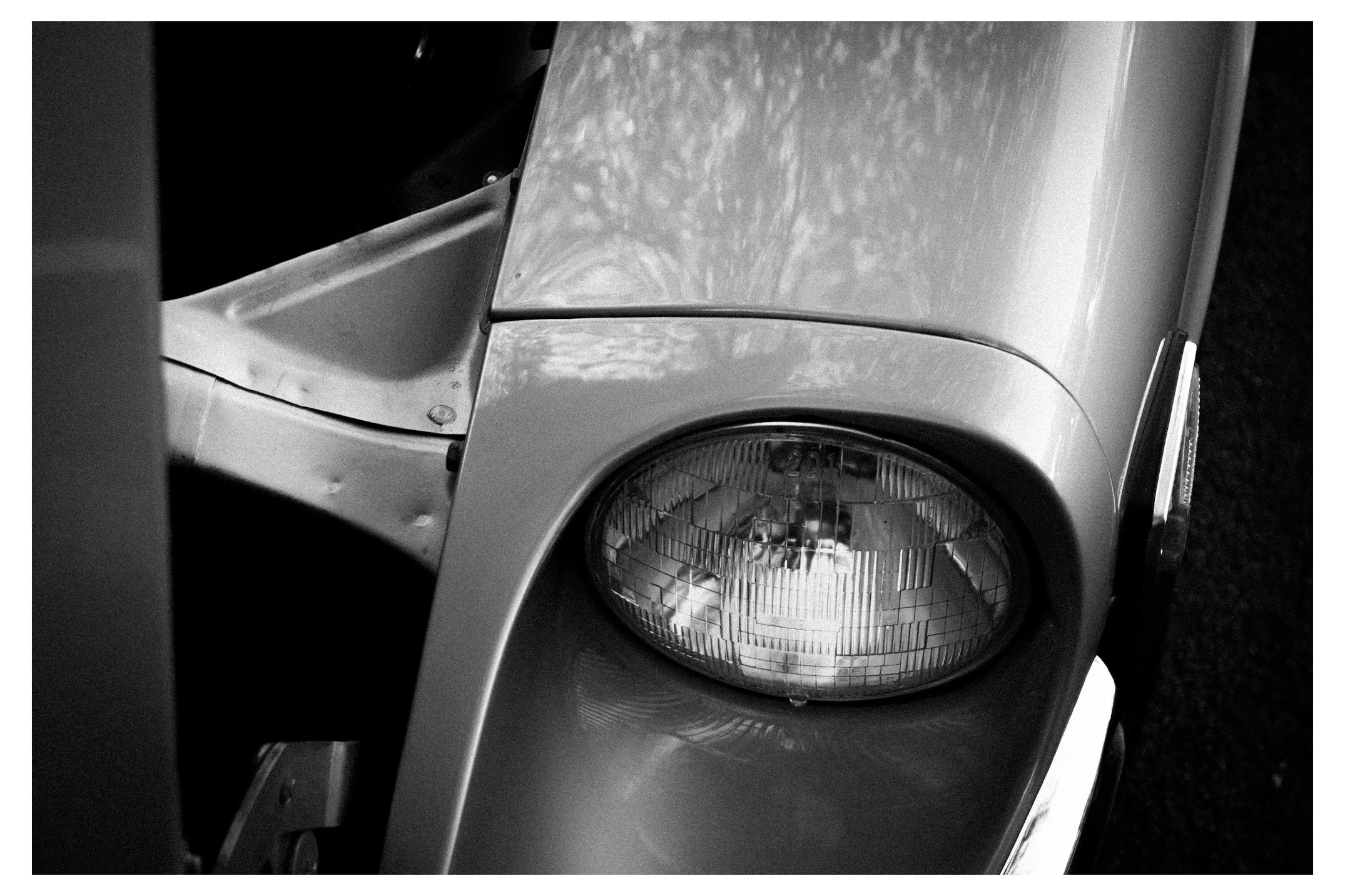 Close-up black and white photo of front part of a washing machine, showing the circular door with a glass window and metal frame.
