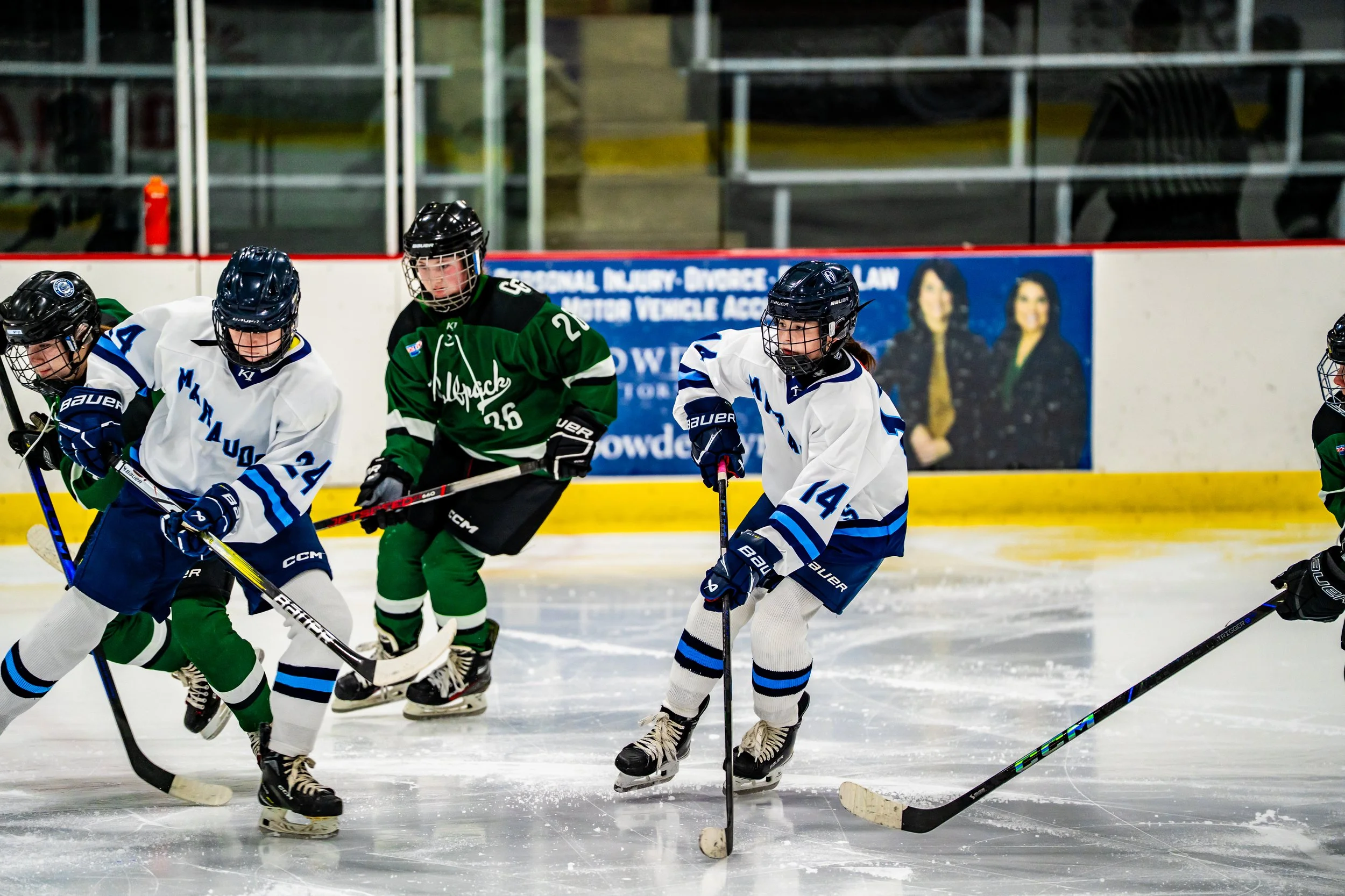Hockey players in white and green jerseys competing on an ice rink during a game.