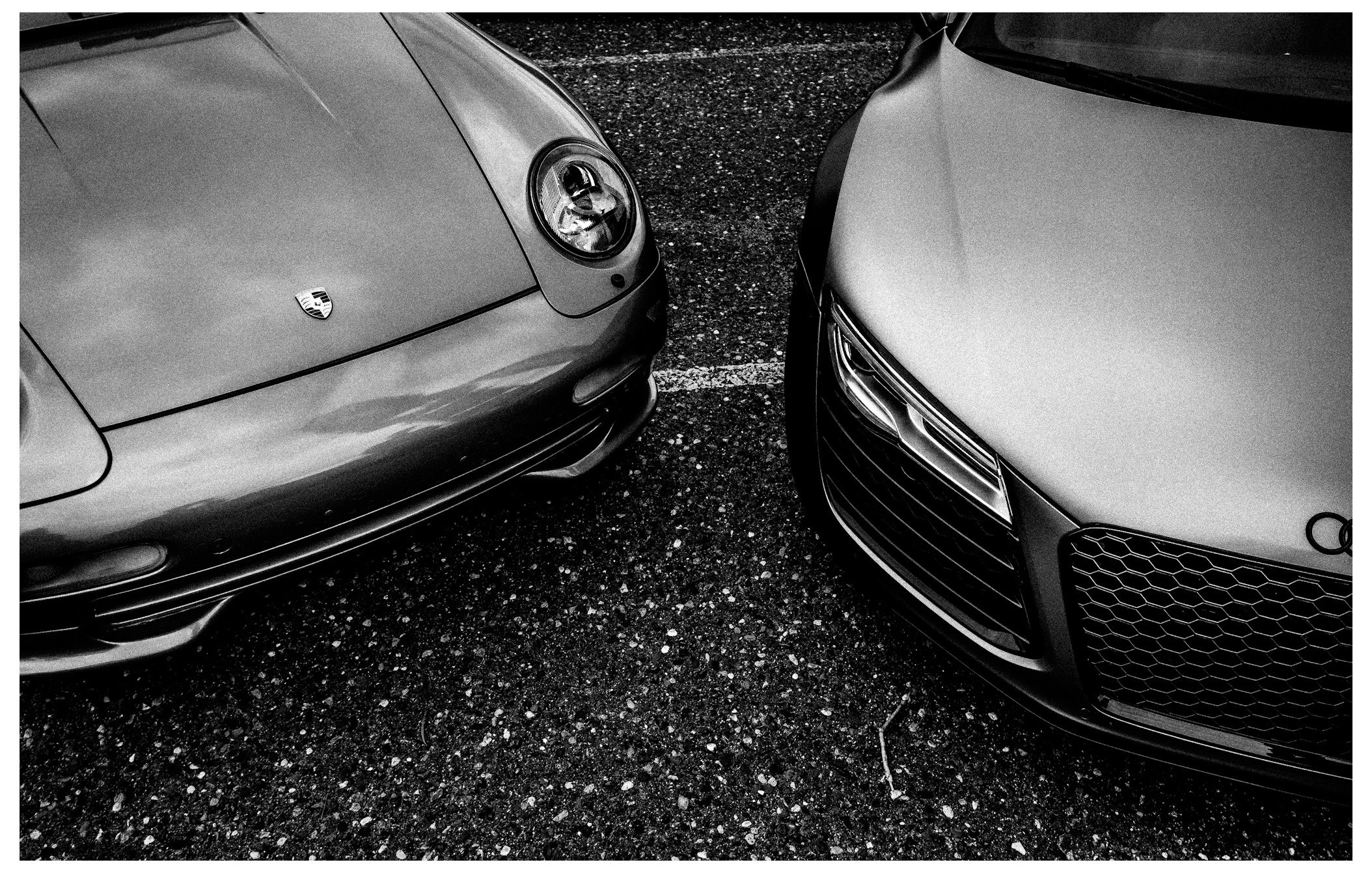 Two cars parked side by side on a textured asphalt surface, one on the left and one on the right.