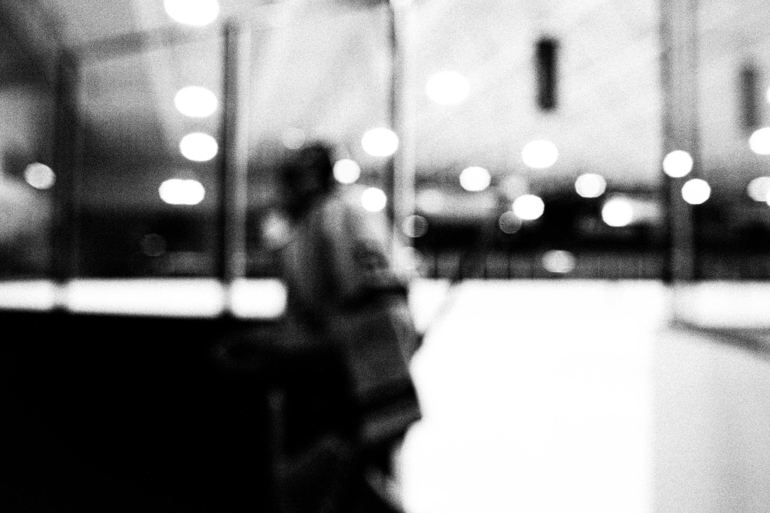 Black and white blurred image of a person in what appears to be a brightly lit indoor environment.