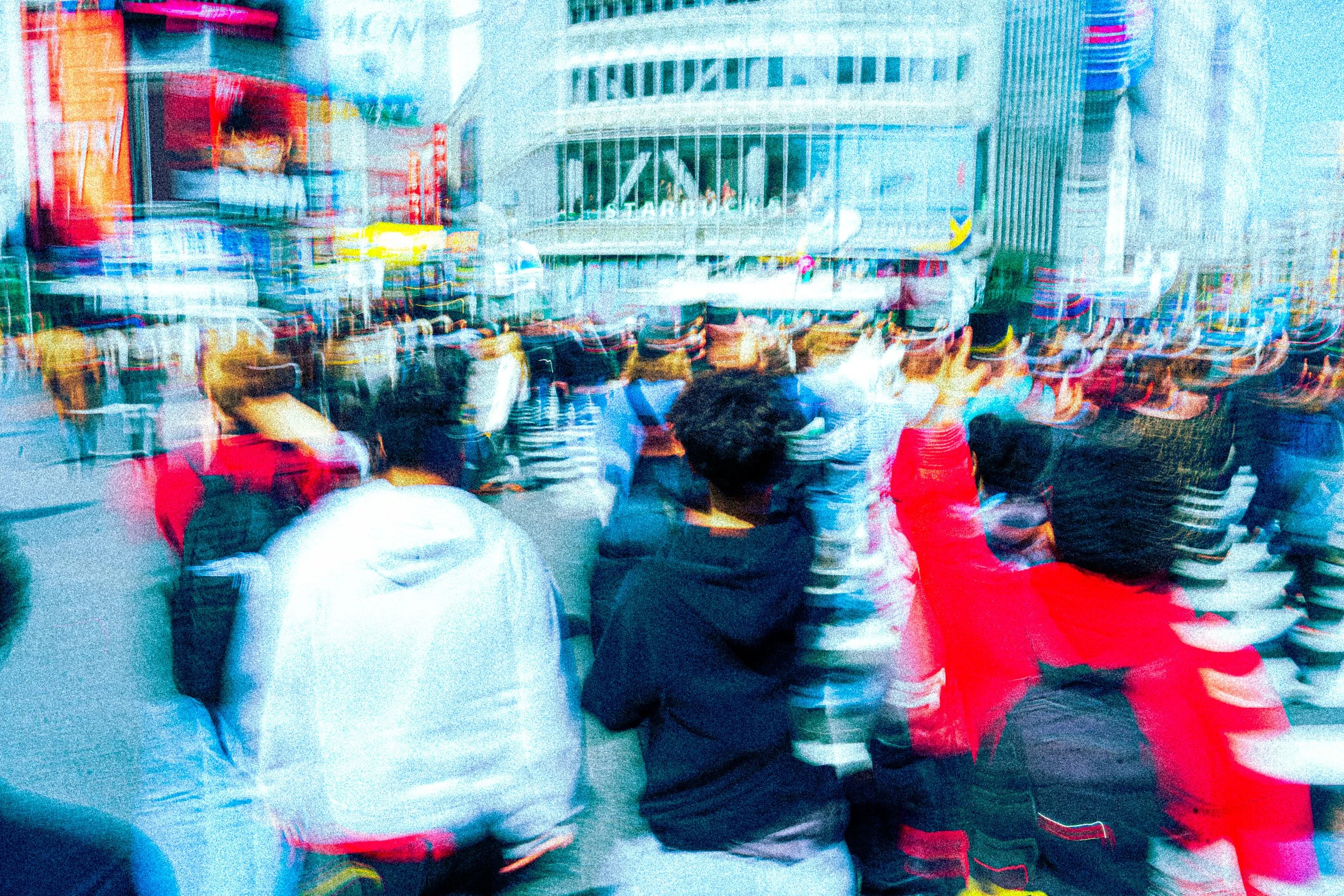 Crowd of people gathered outdoors in front of tall buildings on a city street.