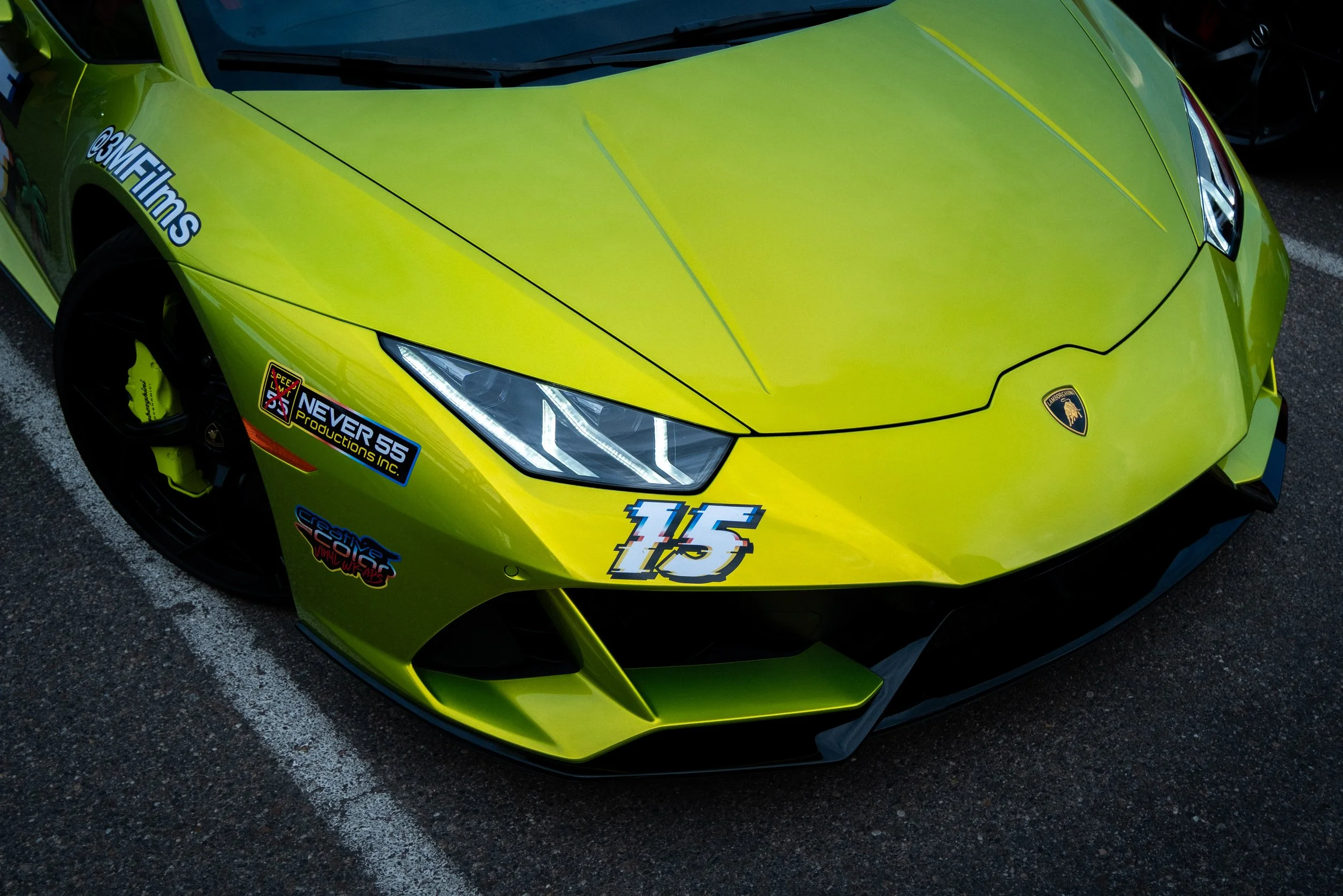 A bright yellow Lamborghini sports car with racing stickers, parked on a parking lot marked with white lines.