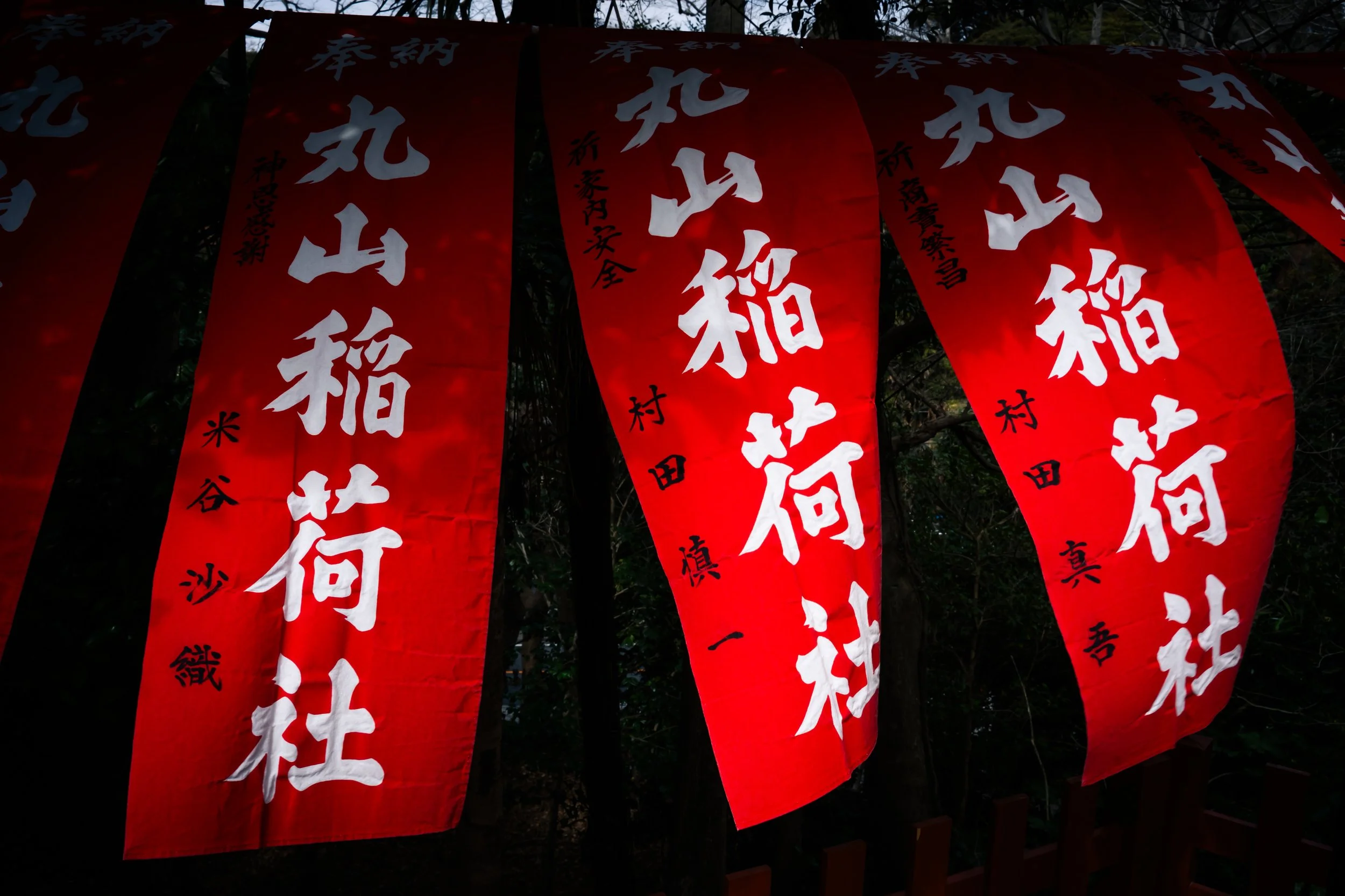 Red banners with white Japanese characters hanging outdoors, likely in a forested area.