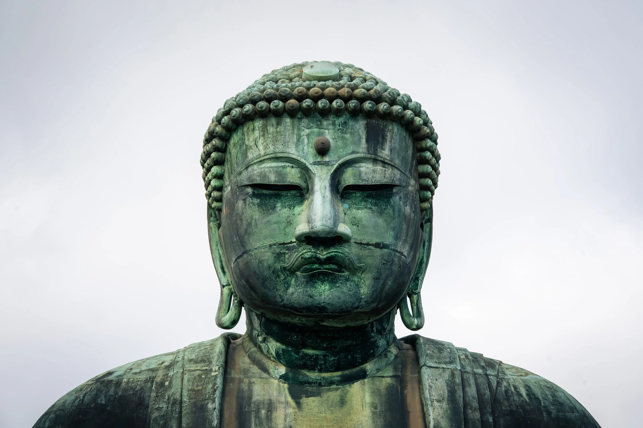Close-up of a large bronze statue of Buddha's head and upper torso against a cloudy sky.