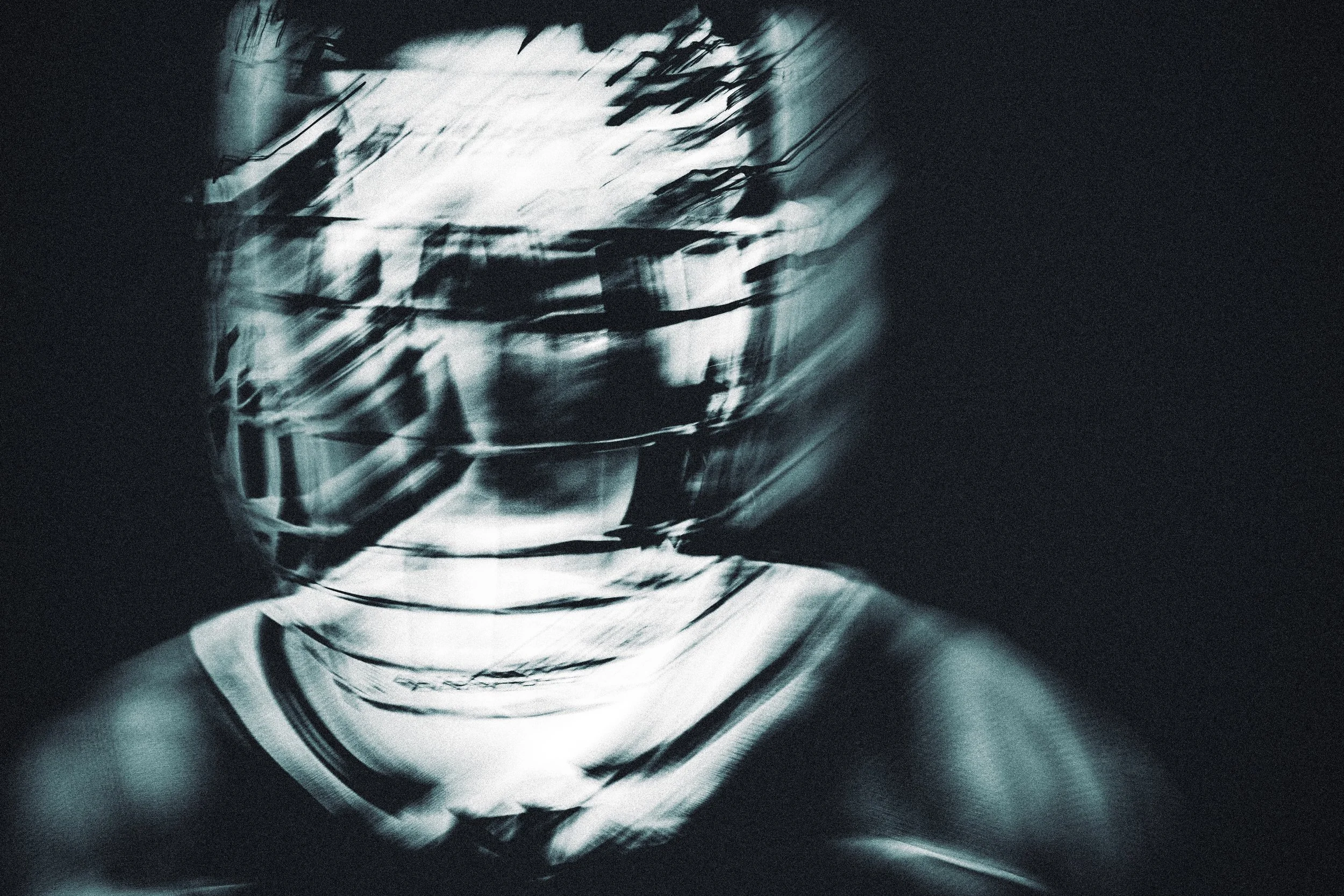 A distorted reflection of a person’s face in a glass or metallic surface, with abstract, streaked black and white patterns.