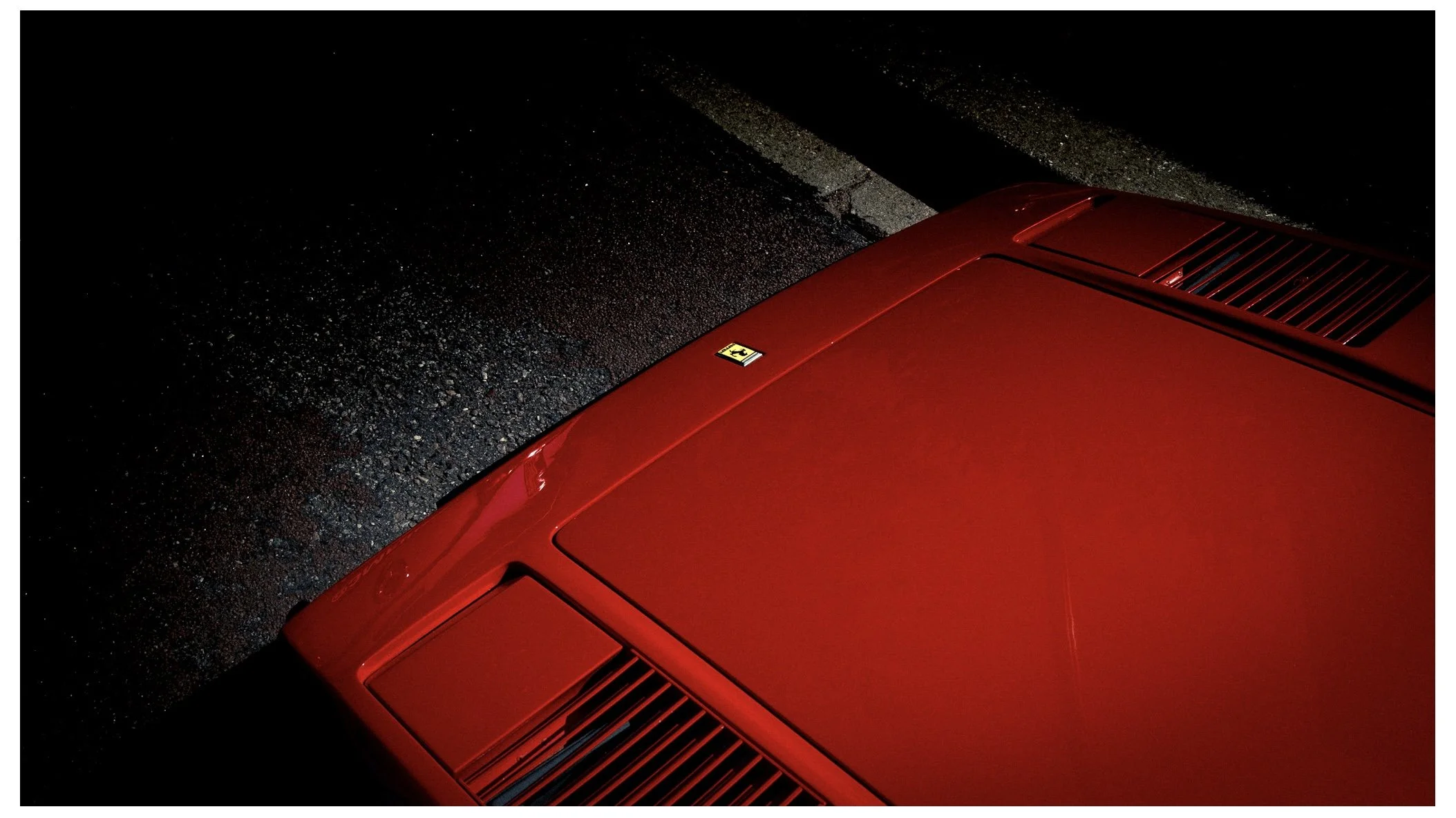 Close-up of the red roof of a car, showing vents and a Ferrari logo, on a dark street at night.