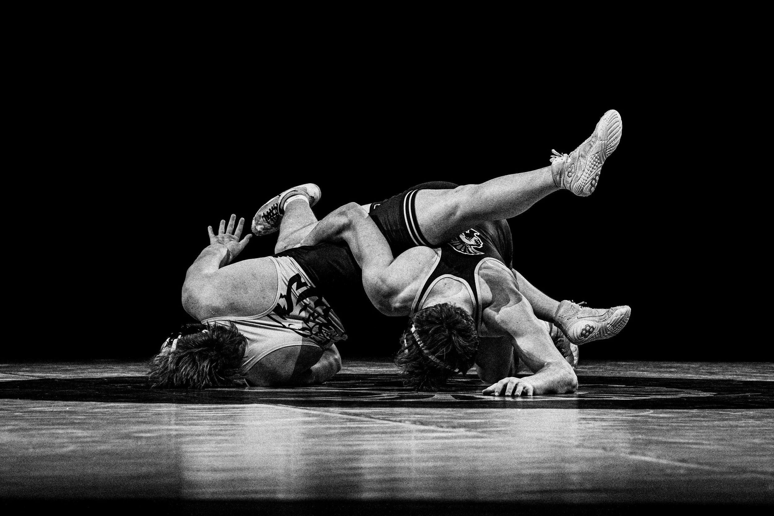 Black and white photo of two wrestlers in a match on a wrestling mat, one wrestler in a dominant position over the other.