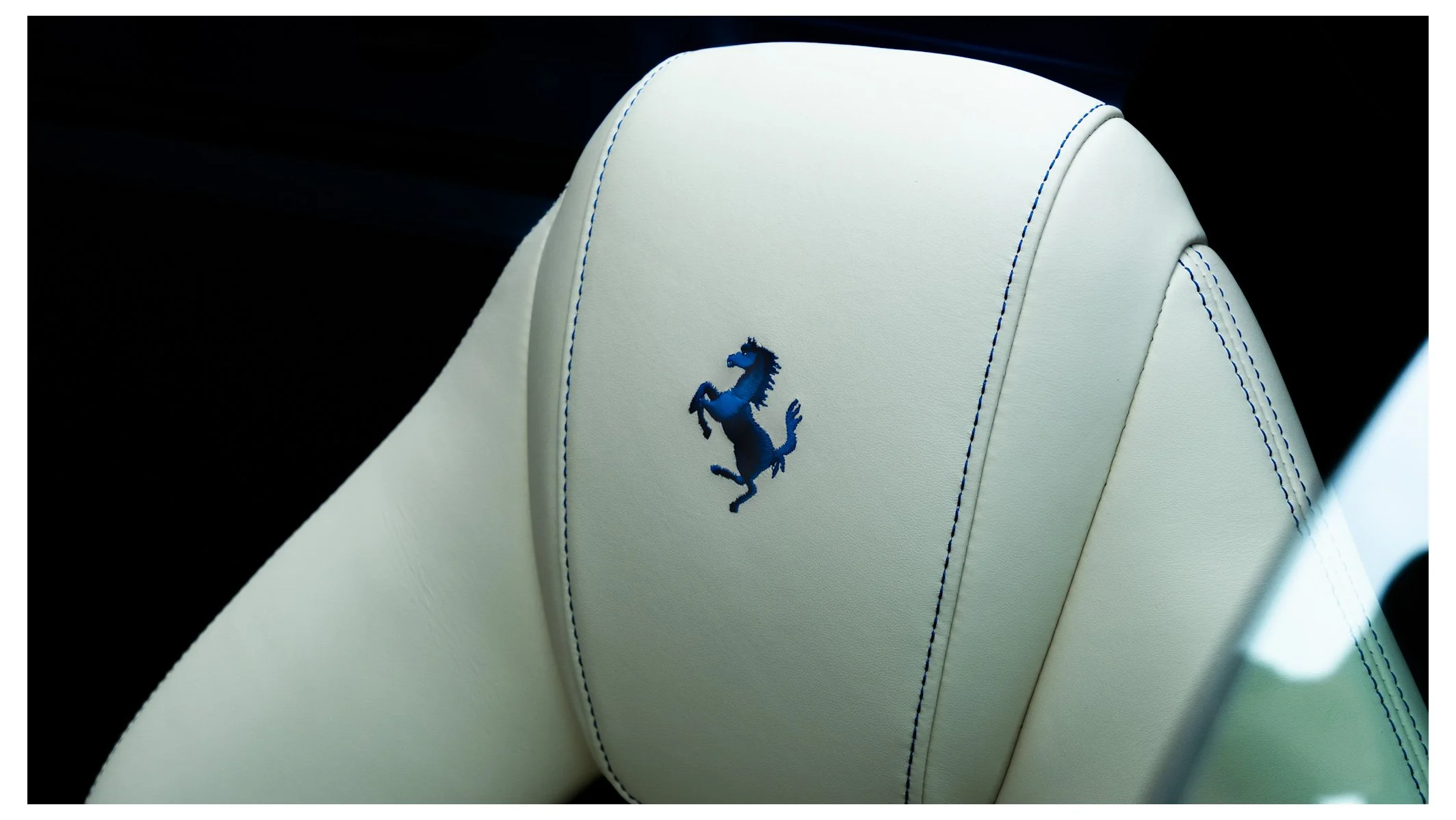 Close-up of a white car seat with blue stitching and the Ferrari logo embroidered in blue.