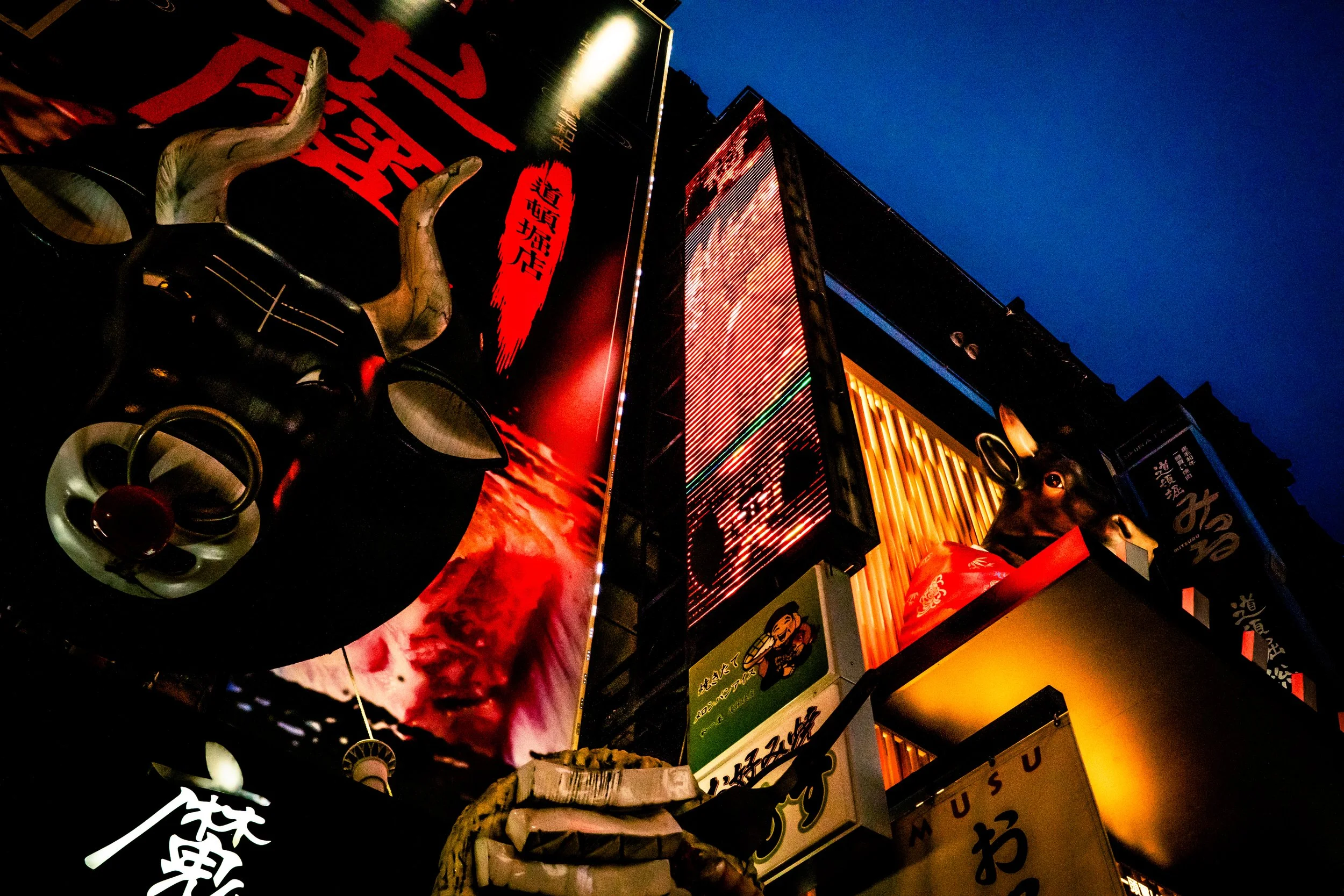 Nighttime street scene with illuminated signs, including a large sign with red Japanese characters and a demonstration of Japanese posters and advertisements.
