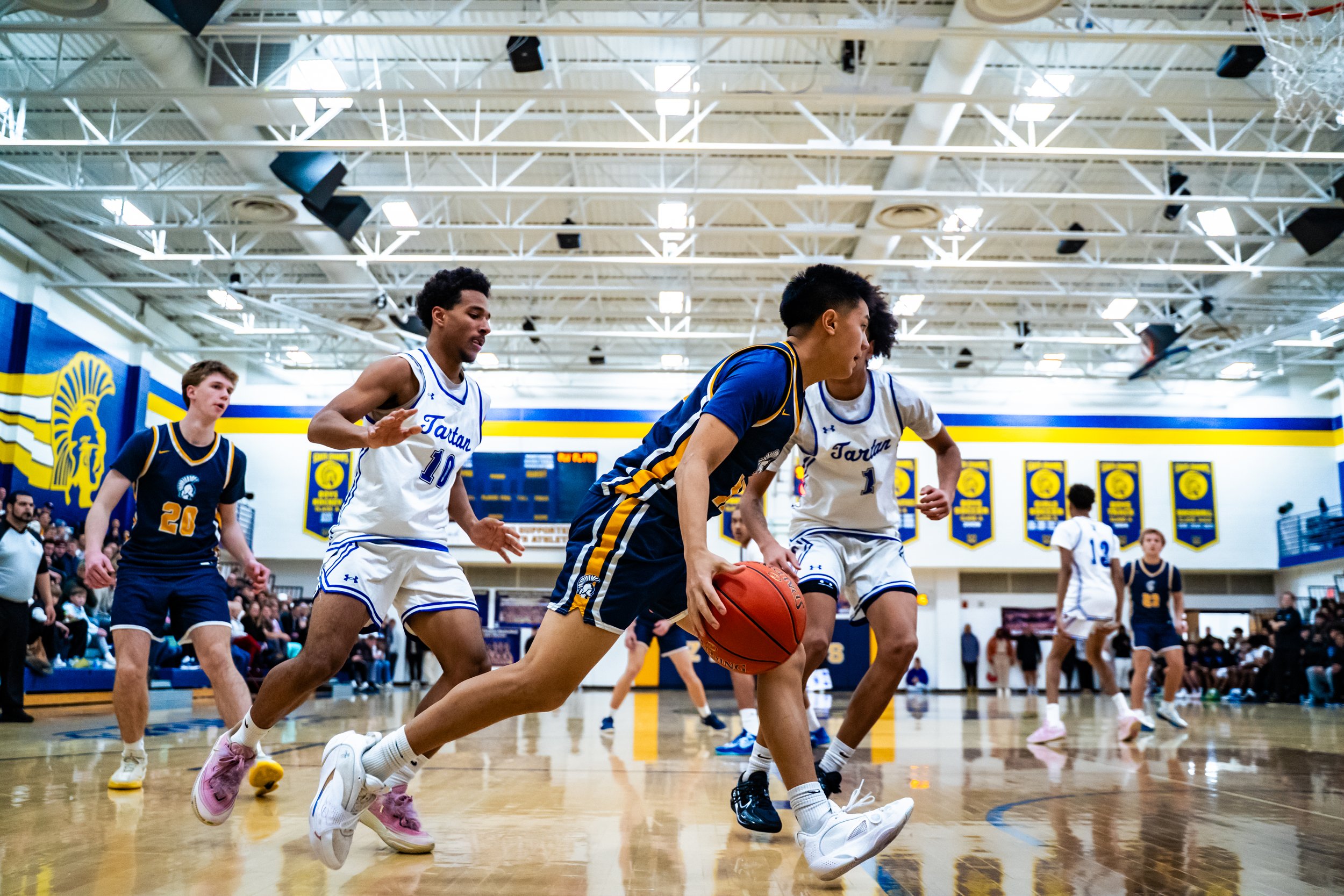 Youth basketball game in a gym with players from two teams, one in white jerseys and the other in dark blue jerseys, chasing the basketball.