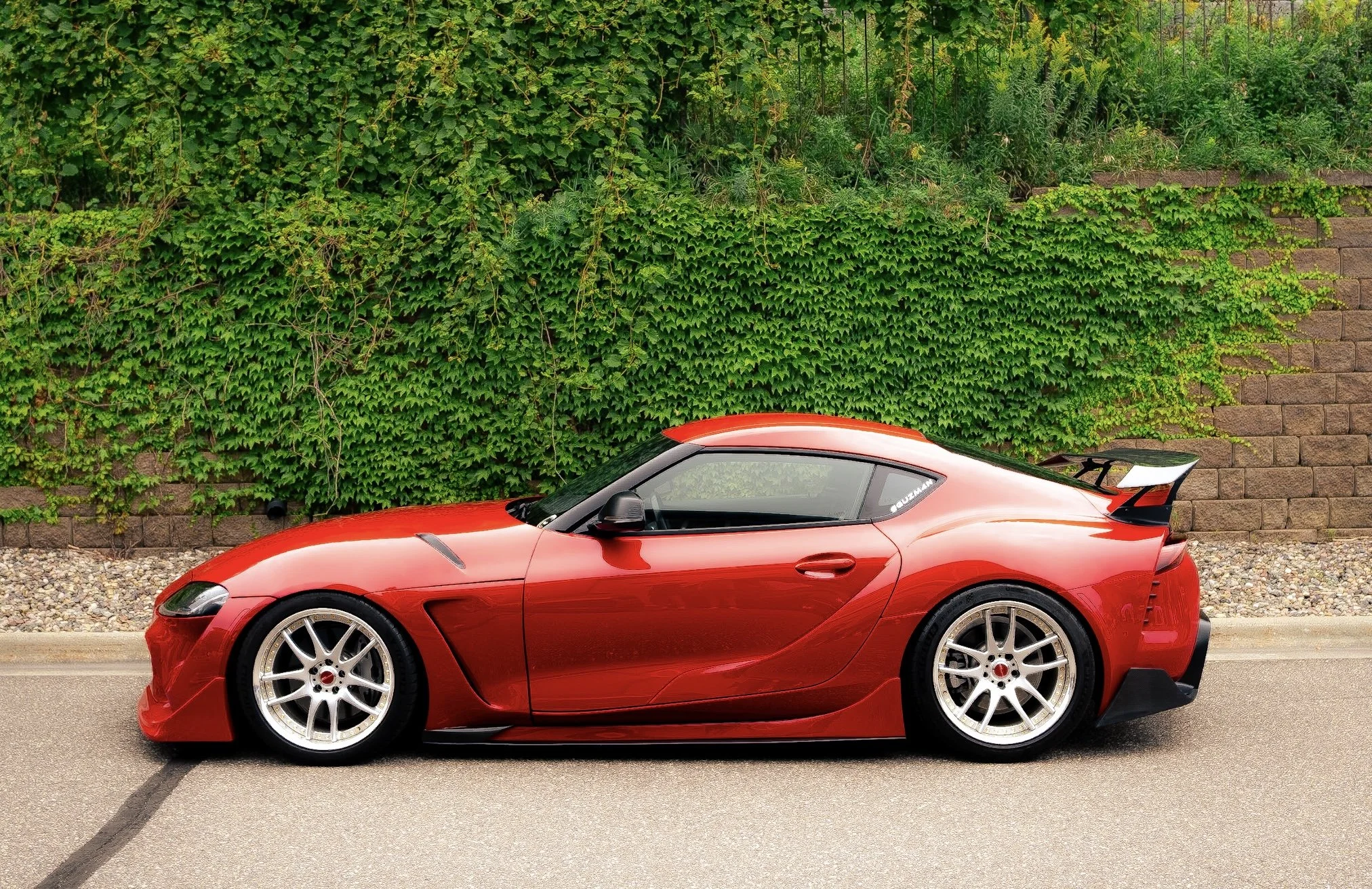 A red sports car parked on the street in front of a green ivy-covered wall.