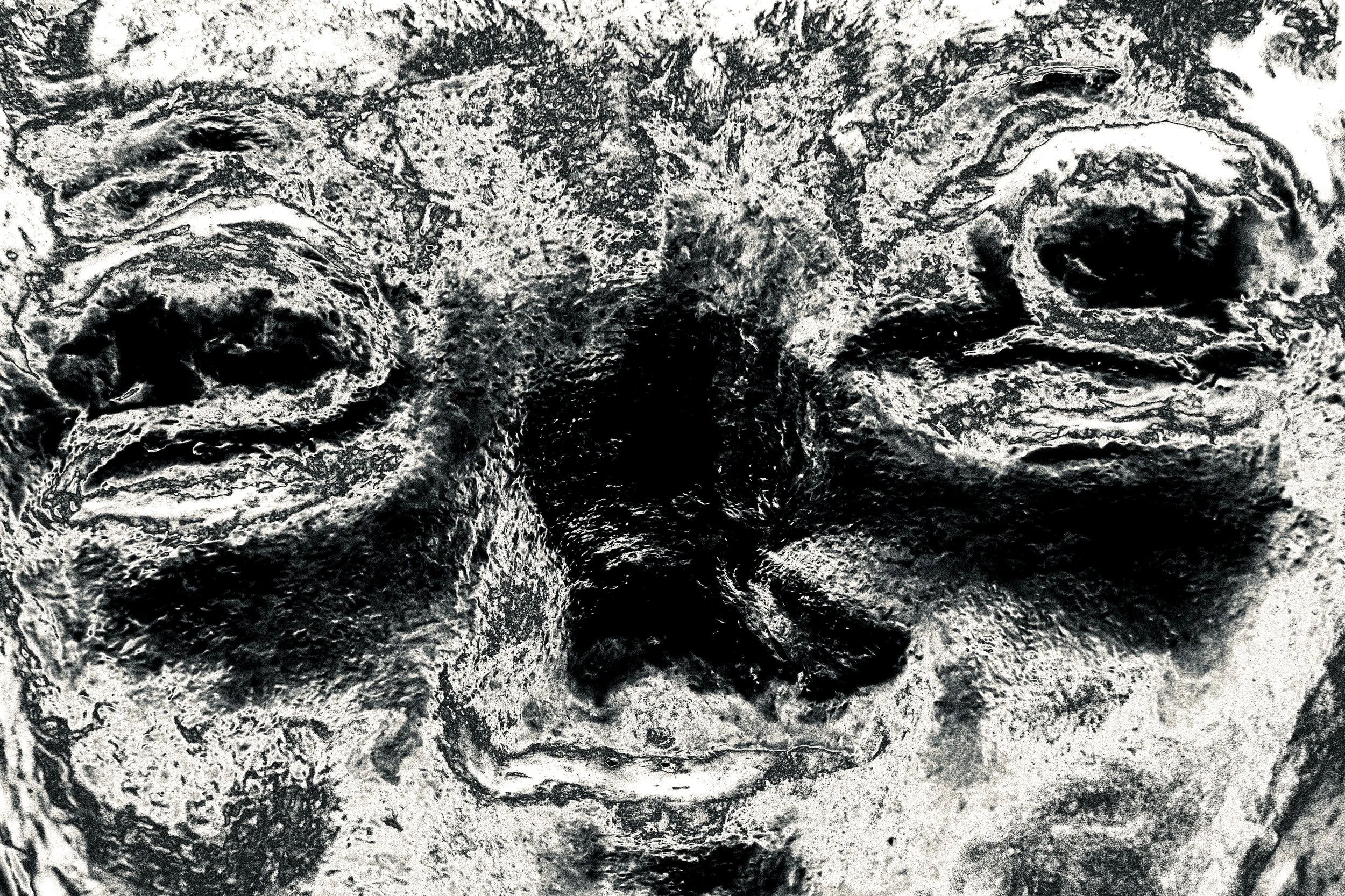 Close-up black and white photo of a textured, rugged rocky surface with cracks and holes.