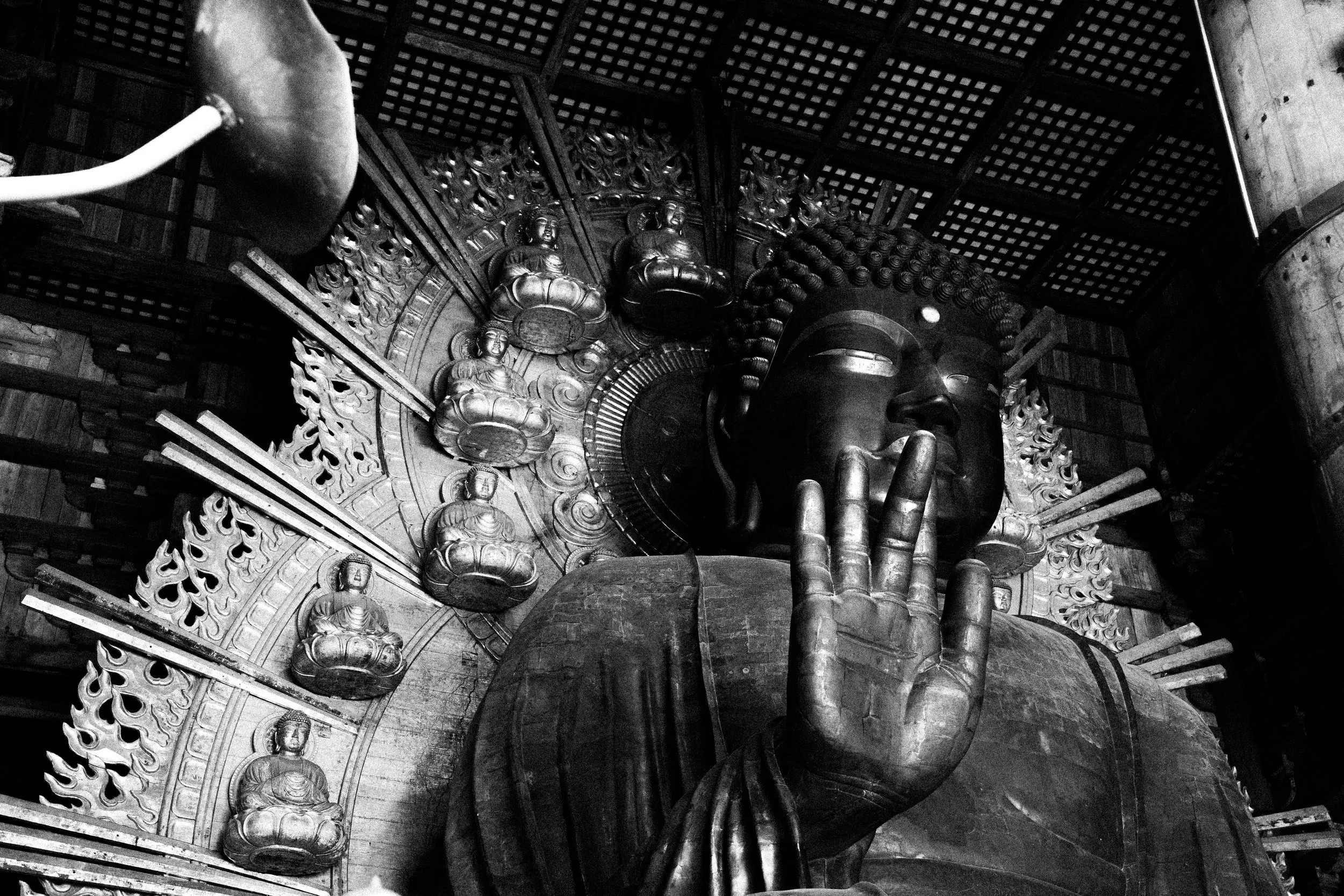 Black and white photo of a Buddhist temple interior with large Buddha statues, intricate wooden carvings, and a spiral staircase.