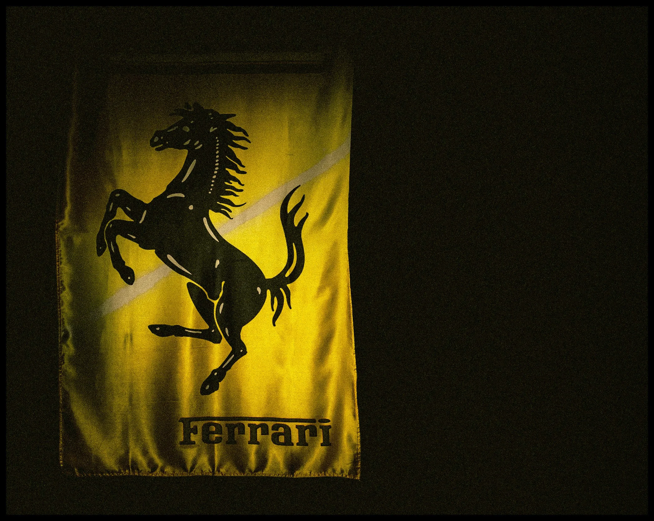 A yellow Ferrari flag featuring a black prancing horse logo, with the word 'Ferrari' at the bottom.