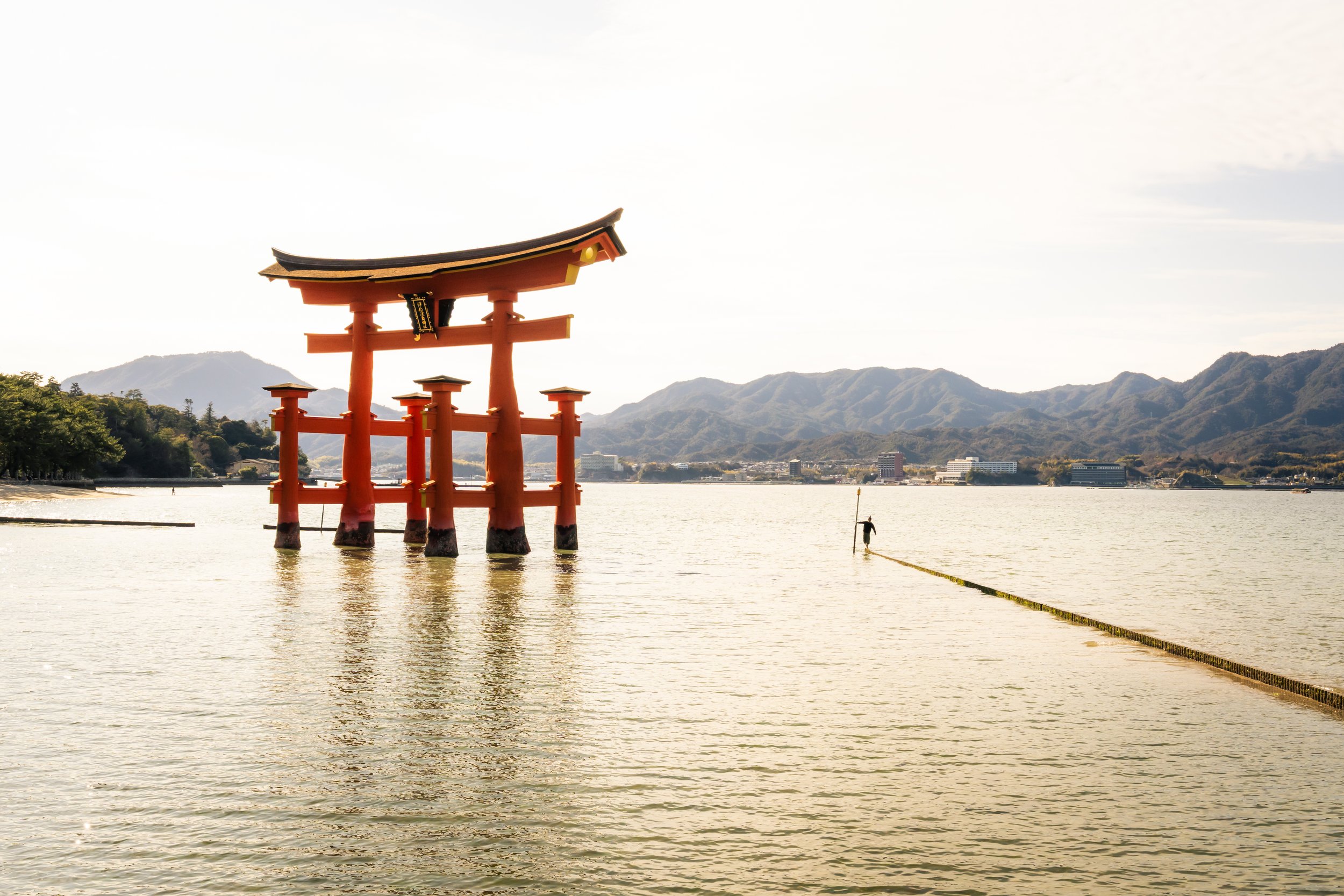 Traditional Japanese torii gate standing in water with mountains in the background.