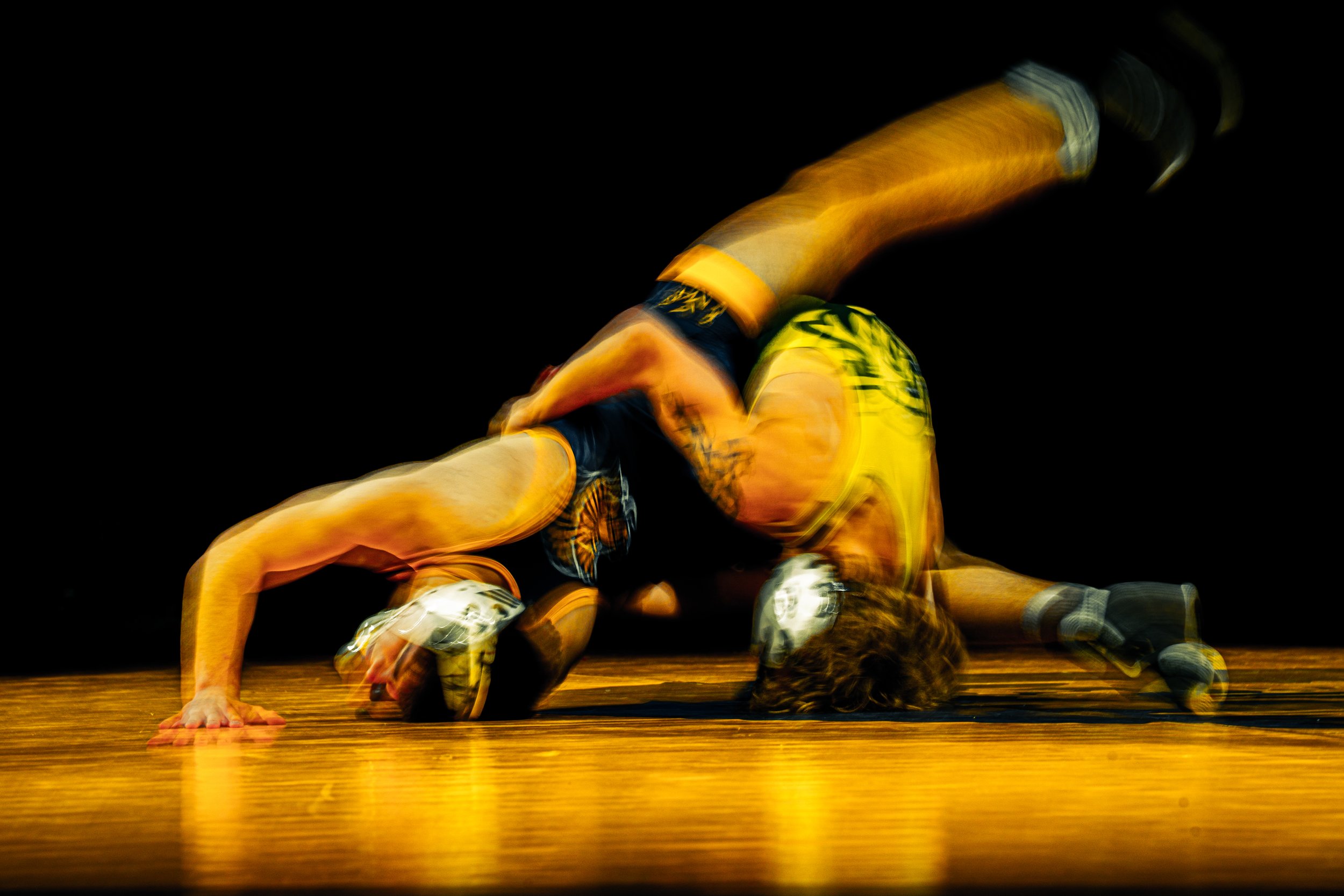 Blurred motion shot of a person in athletic clothing performing a push-up on a wooden floor against a black background.