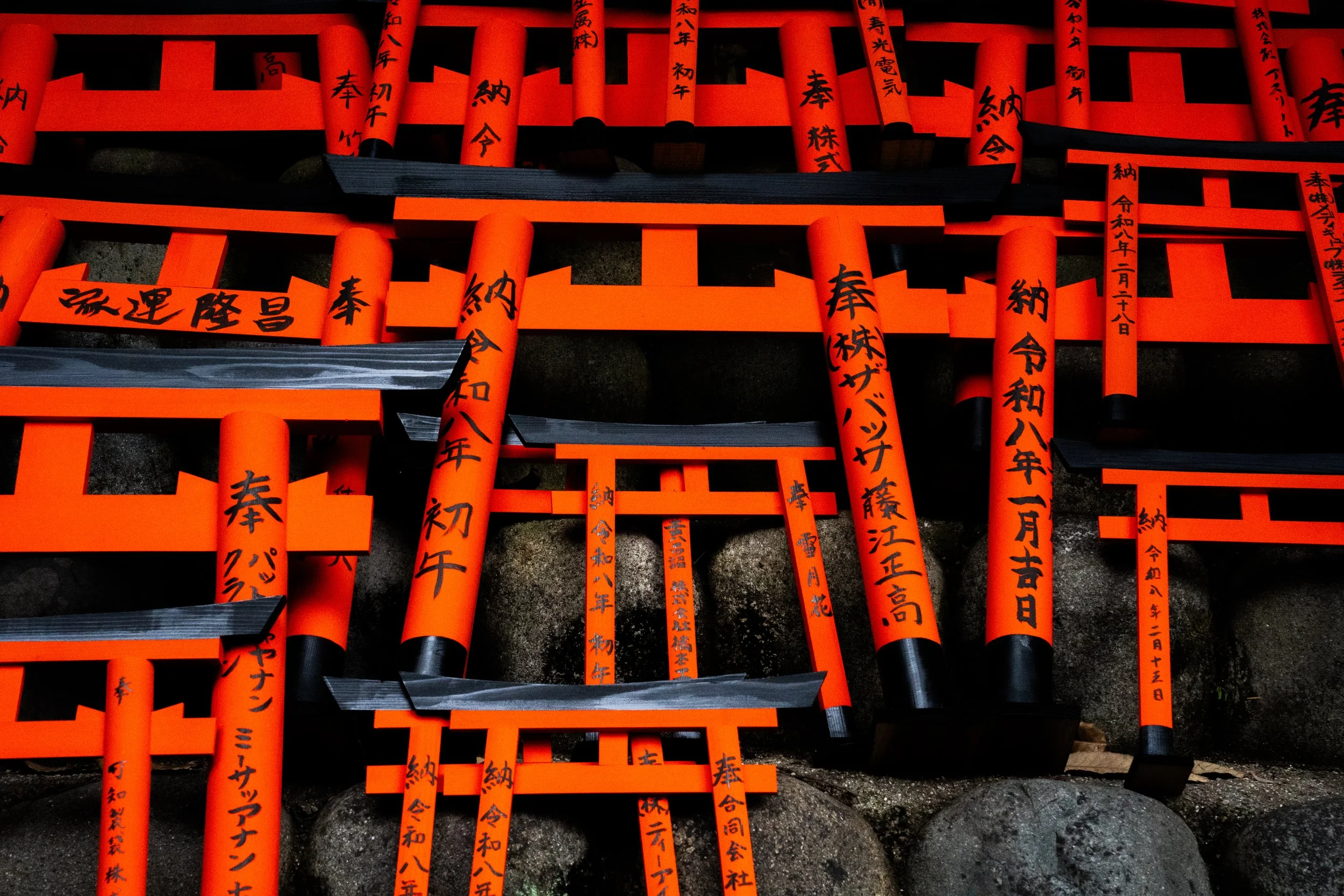 Multiple orange and black wooden torii gates with black and red Japanese calligraphy on their surfaces, arranged in a pathway.