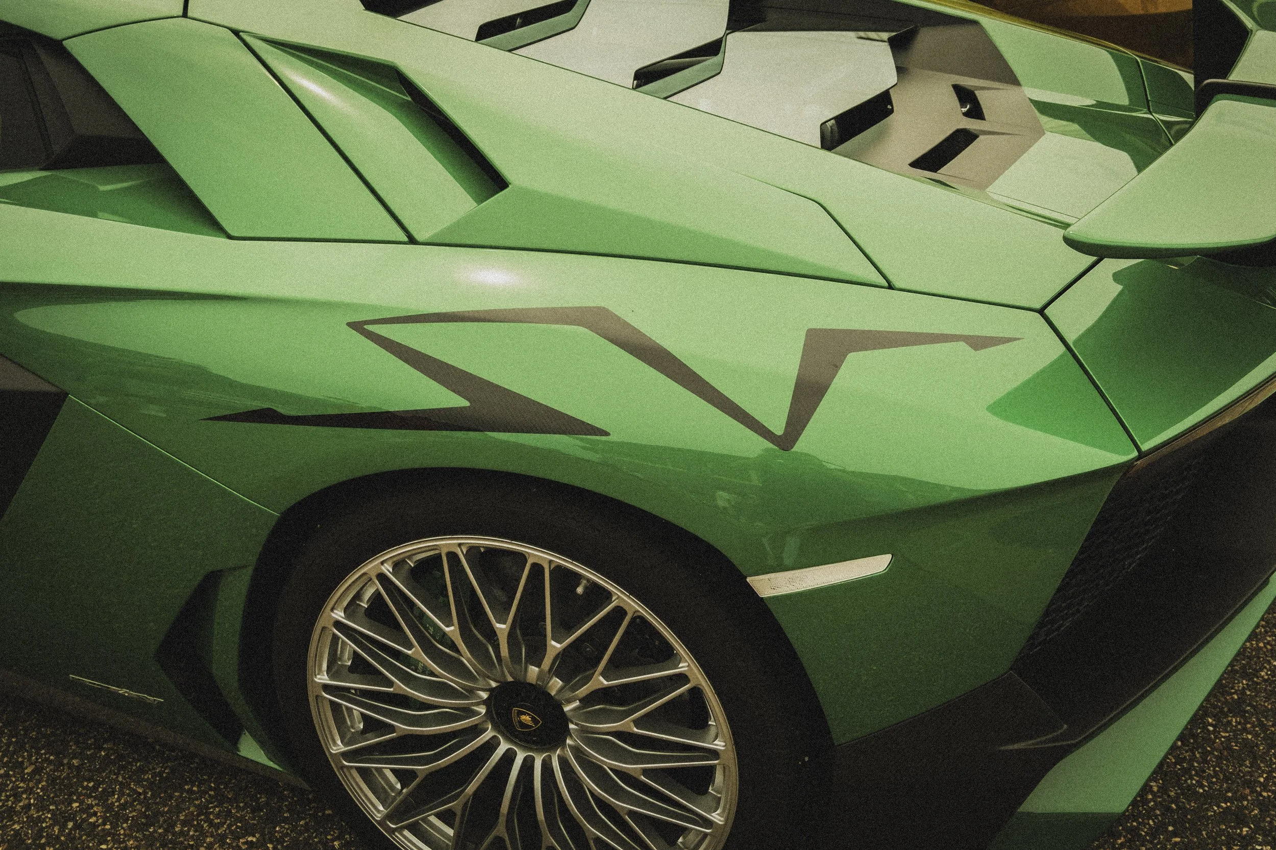 Close-up of a bright green luxury sports car, showing the front left side, wheel, and part of the hood with angular design details.