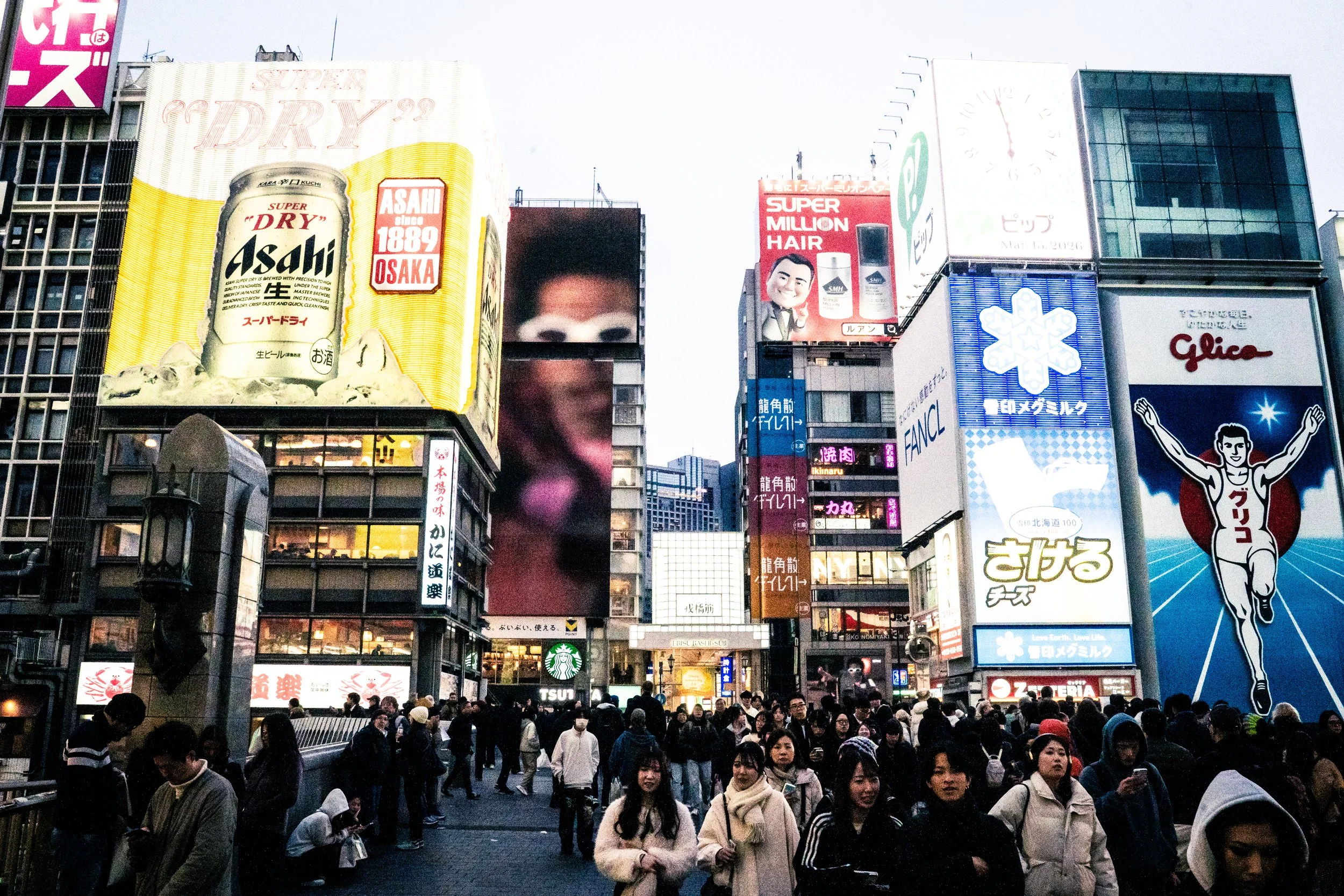 A busy city street scene with digital billboards and advertisements, and a crowd of people walking.