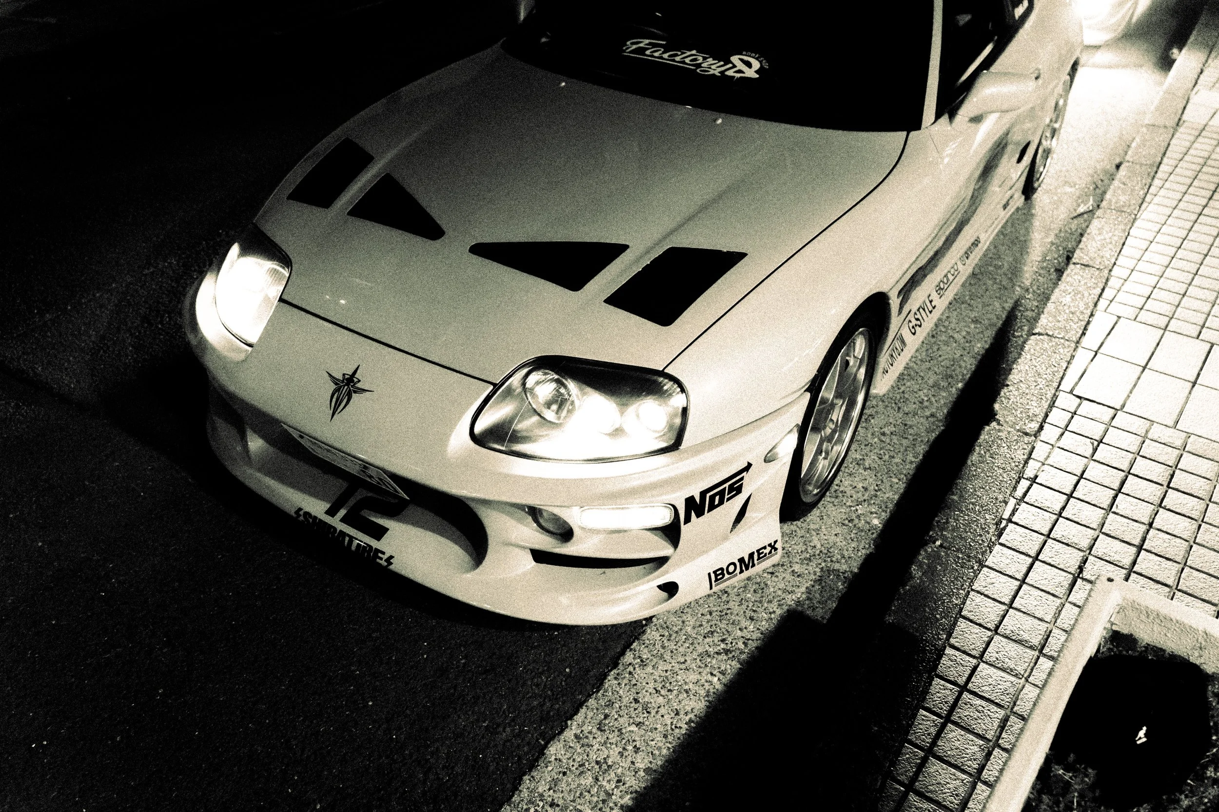 Black sports car with custom decals and stickers parked next to a sidewalk at night.