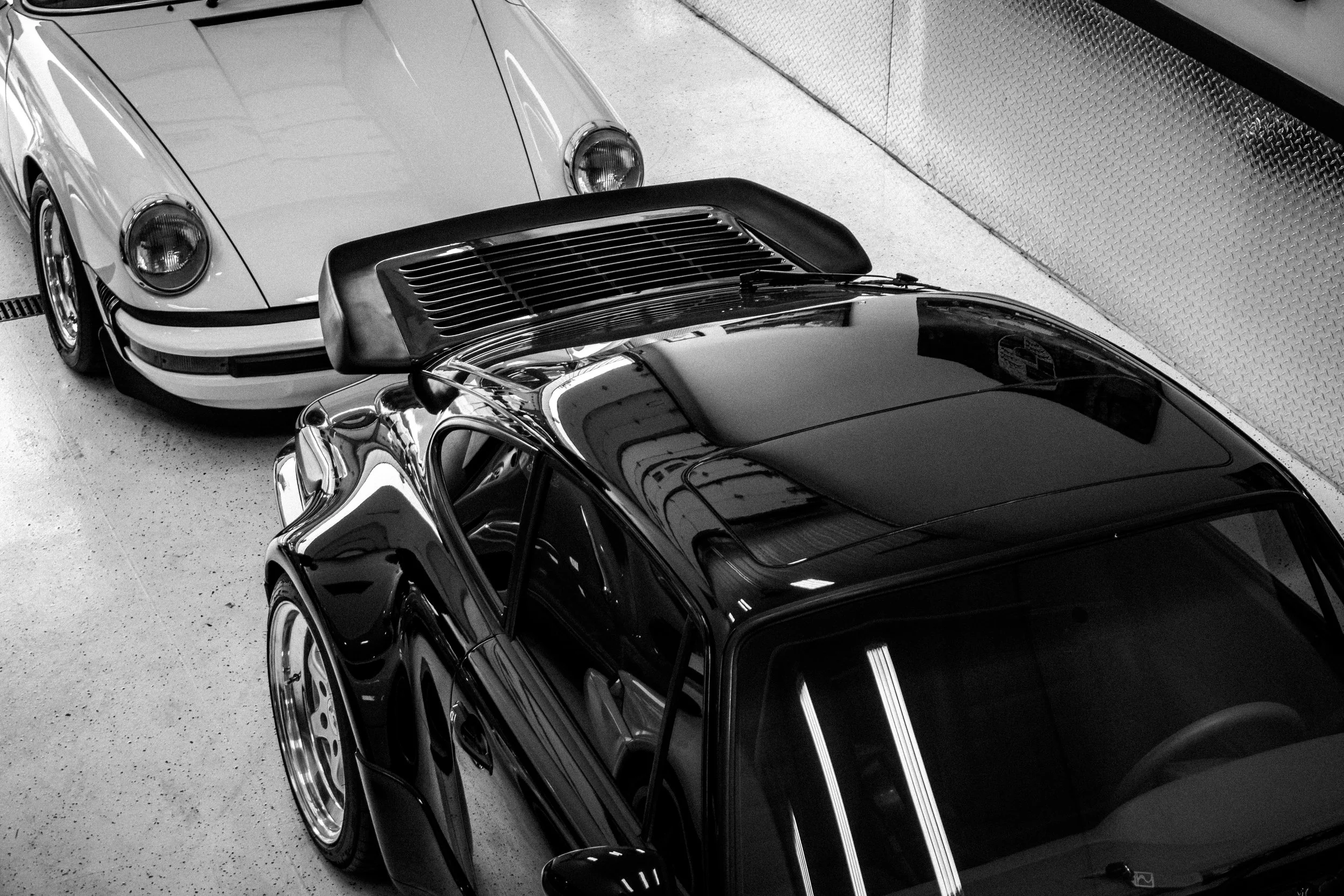Black sports car parked next to a white vintage Porsche in a garage.