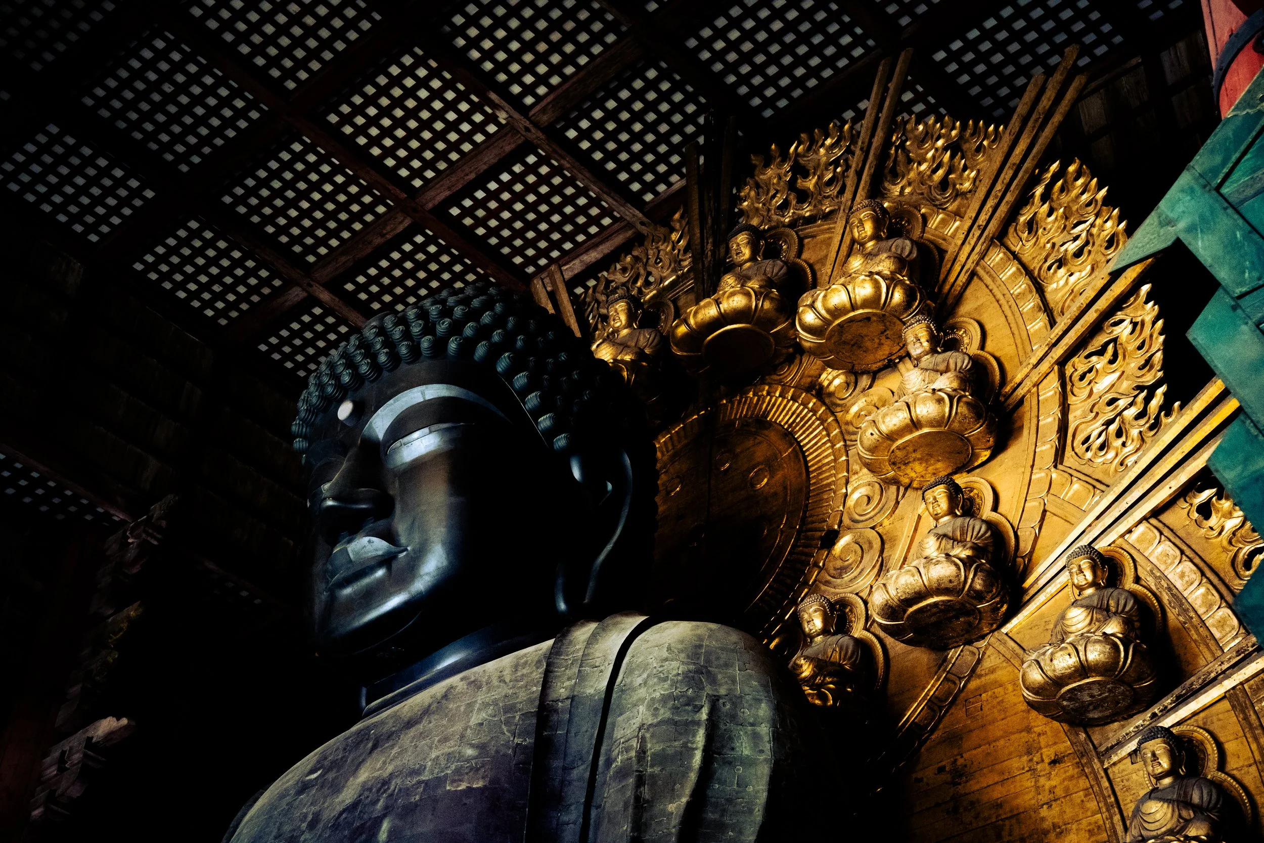 Close-up of a large golden Buddhist or Hindu statue with intricate upturned details, set inside a dimly lit temple with wooden lattice ceiling.