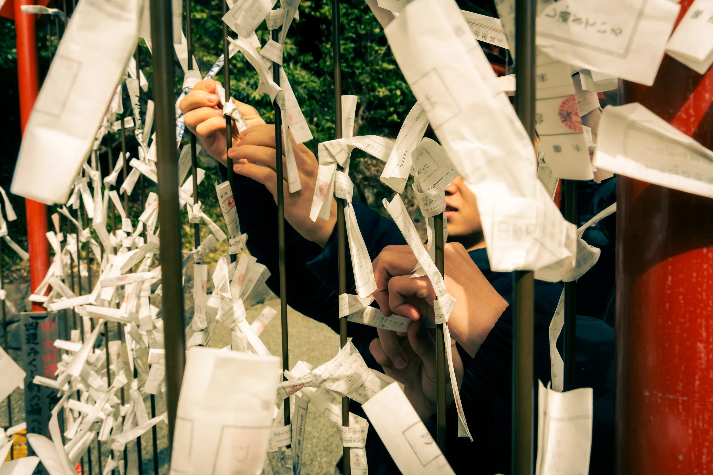 A person placing prayer or wish papers on a metal prayer wall, with many papers attached and green foliage in the background.