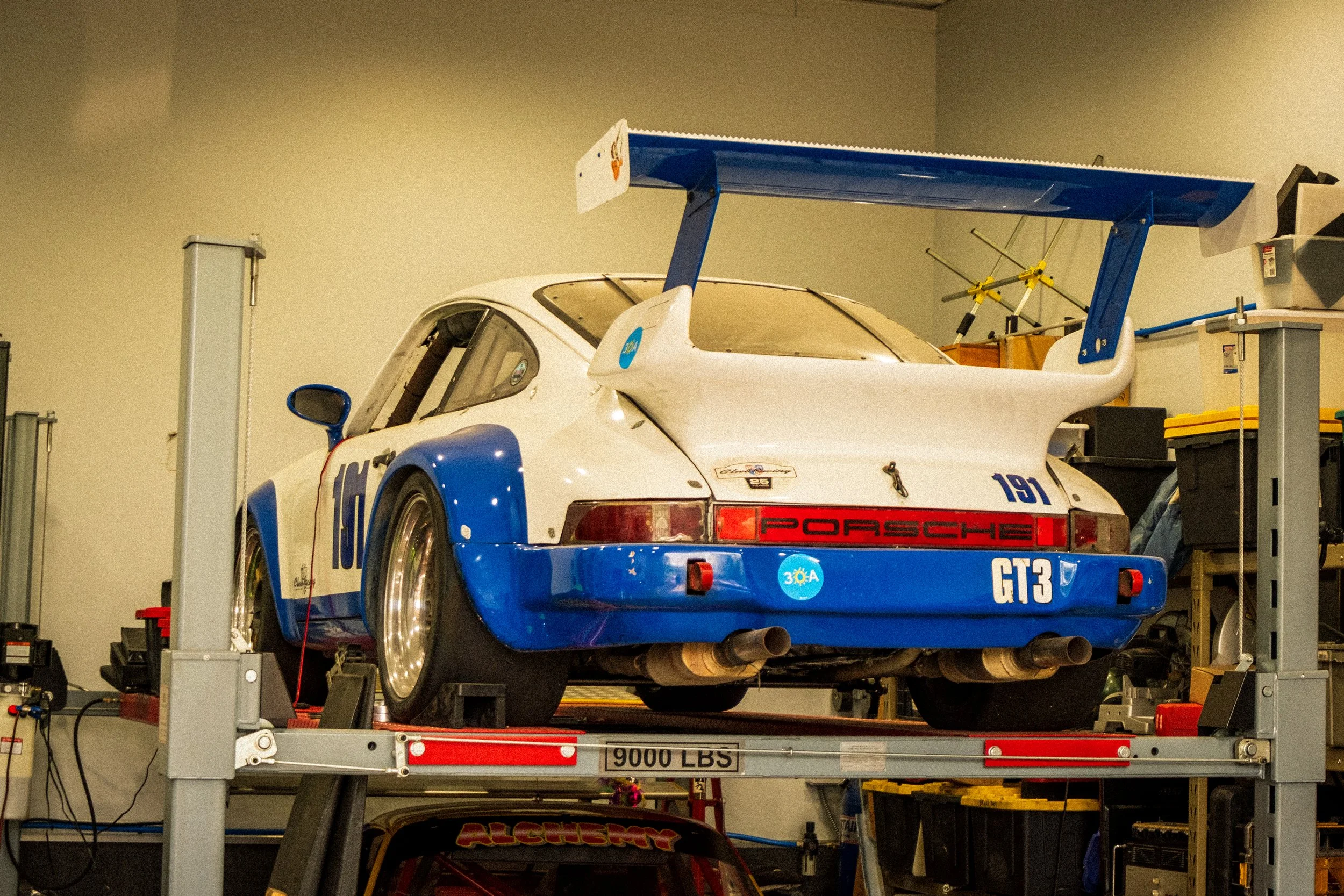 A race car on a lift in a garage, with various tools and equipment around it.