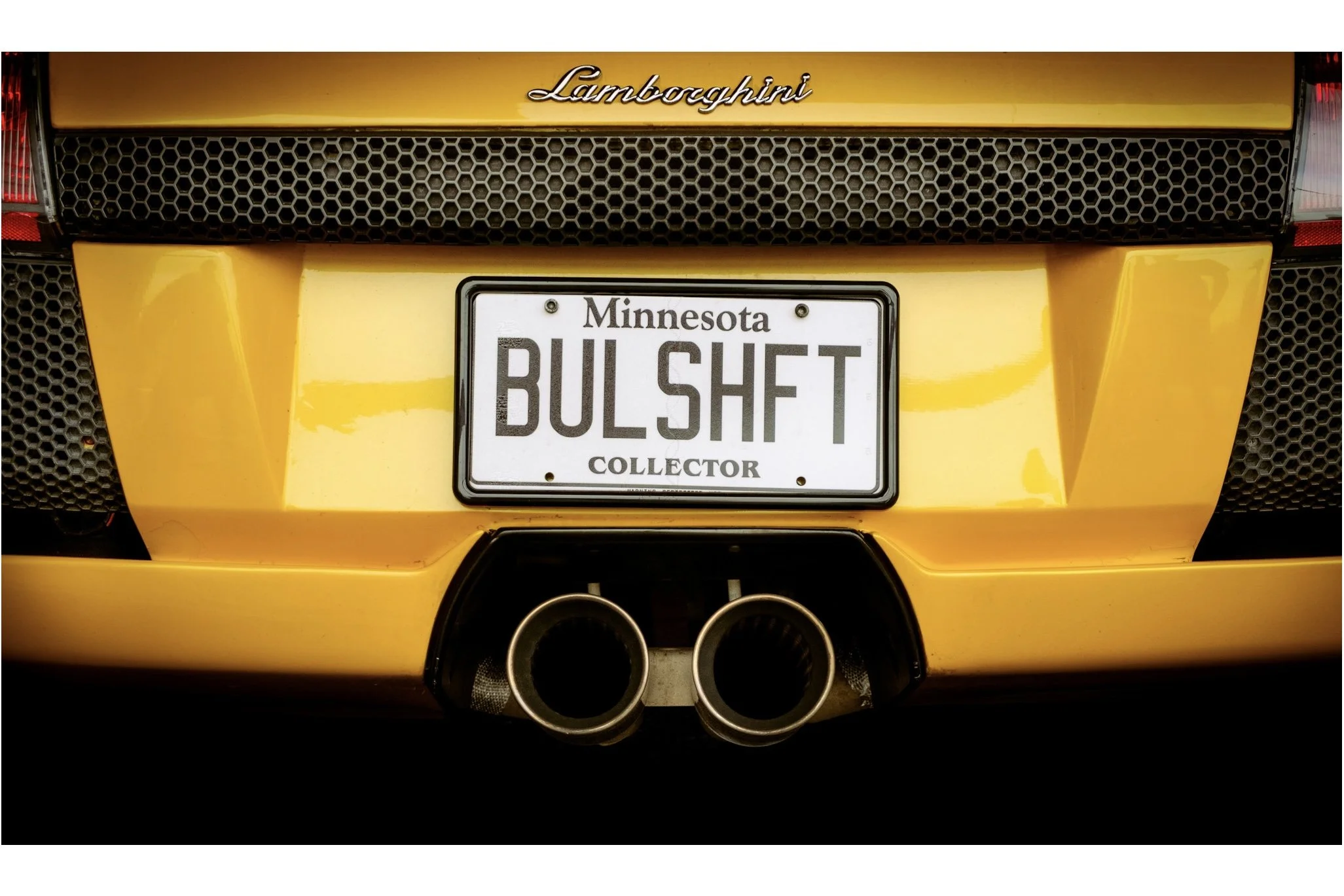 Rear view of a yellow Lamborghini sports car with a Minnesota collector license plate reading 'BULSHIT' and prominent exhaust pipes.