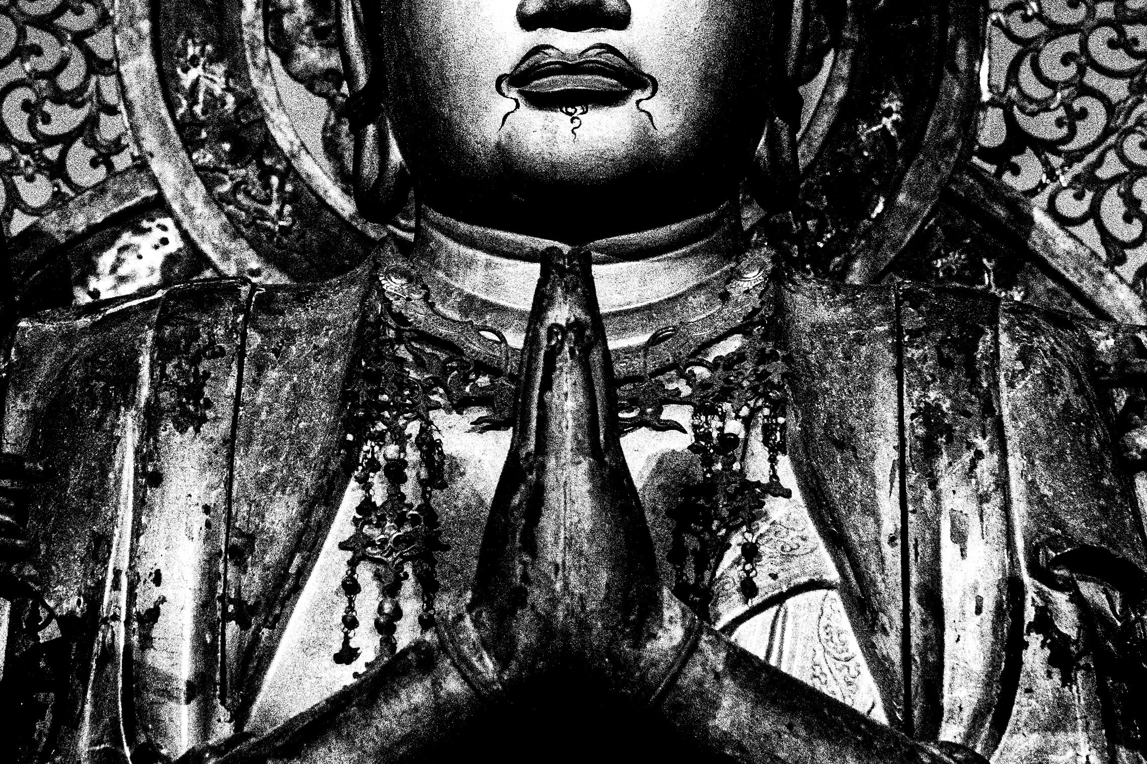 Black and white image of a person with their hands in a praying position, wearing ornate jewelry, with decorative lace behind them.