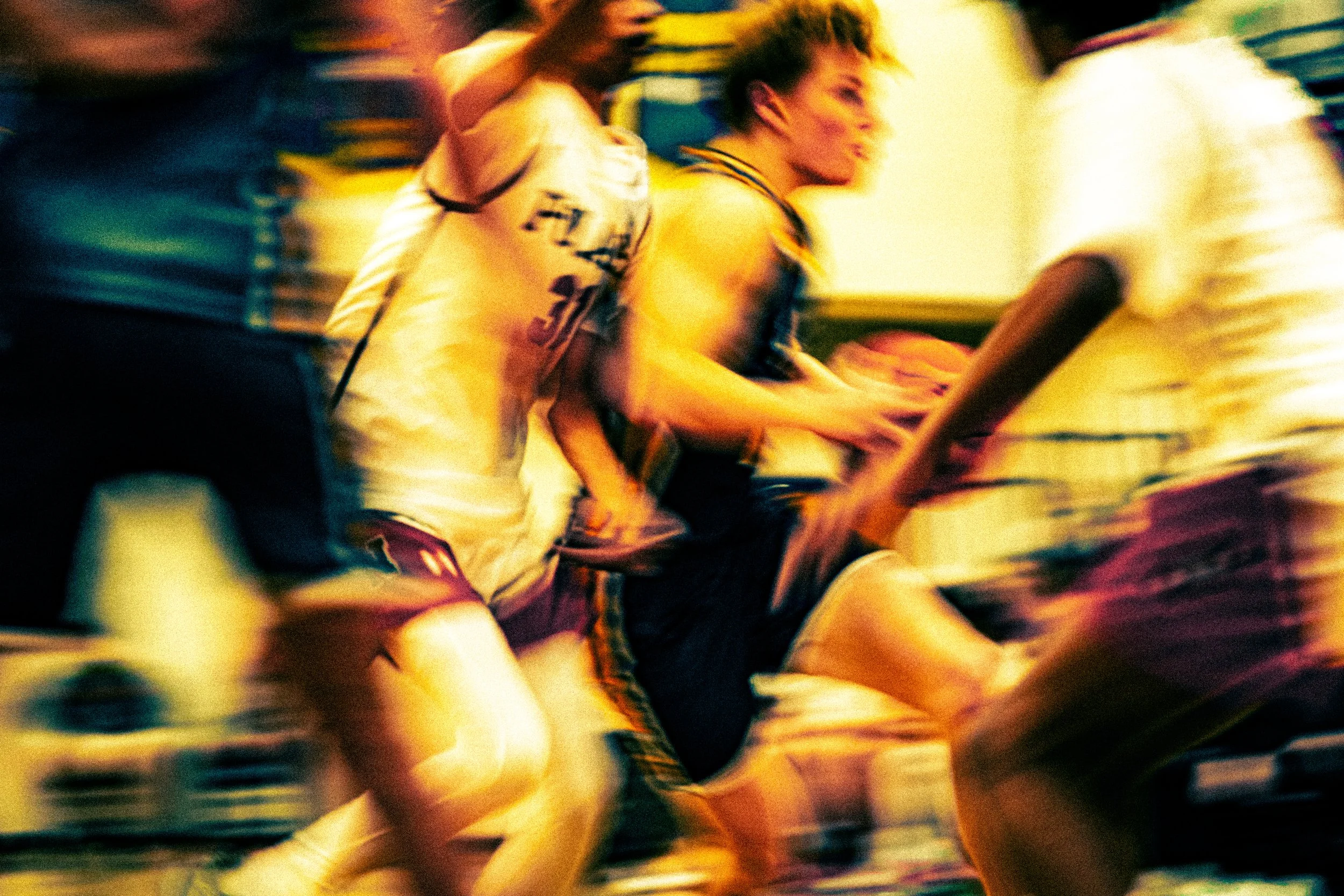 Blurred image of a person with short hair in a sporty outfit, possibly playing a game or participating in an event, with other people around in a lively environment.