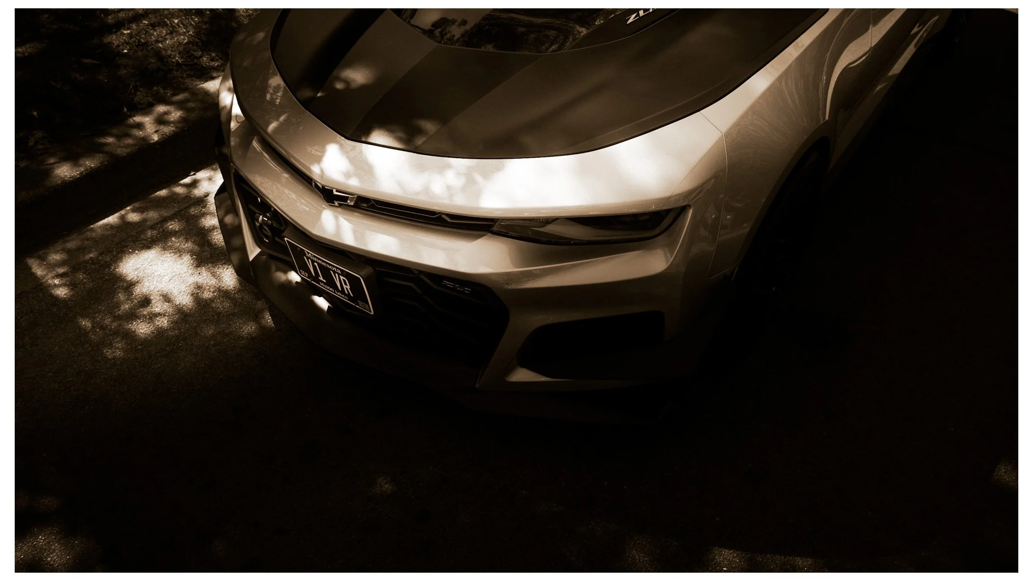 A silver Honda Civic parked on a dirt surface with shadows from foliage on the ground and car.