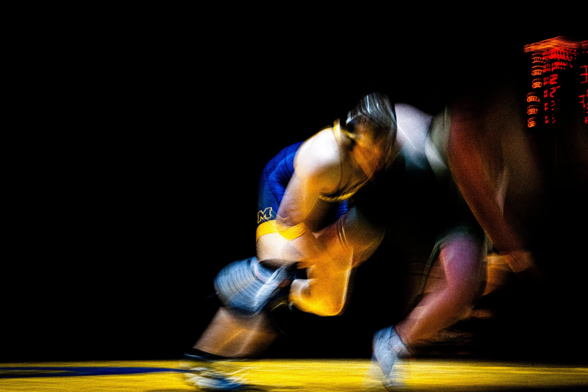 A male athlete wearing a helmet and sports uniform in a dark setting, with digital display lights and streaks of light in the background.