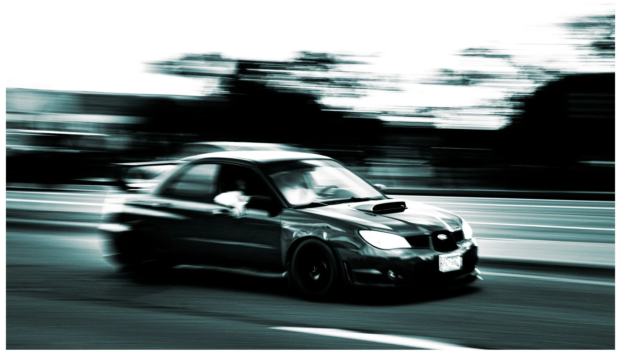 A blurred image of a car driving on a highway with trees in the background.